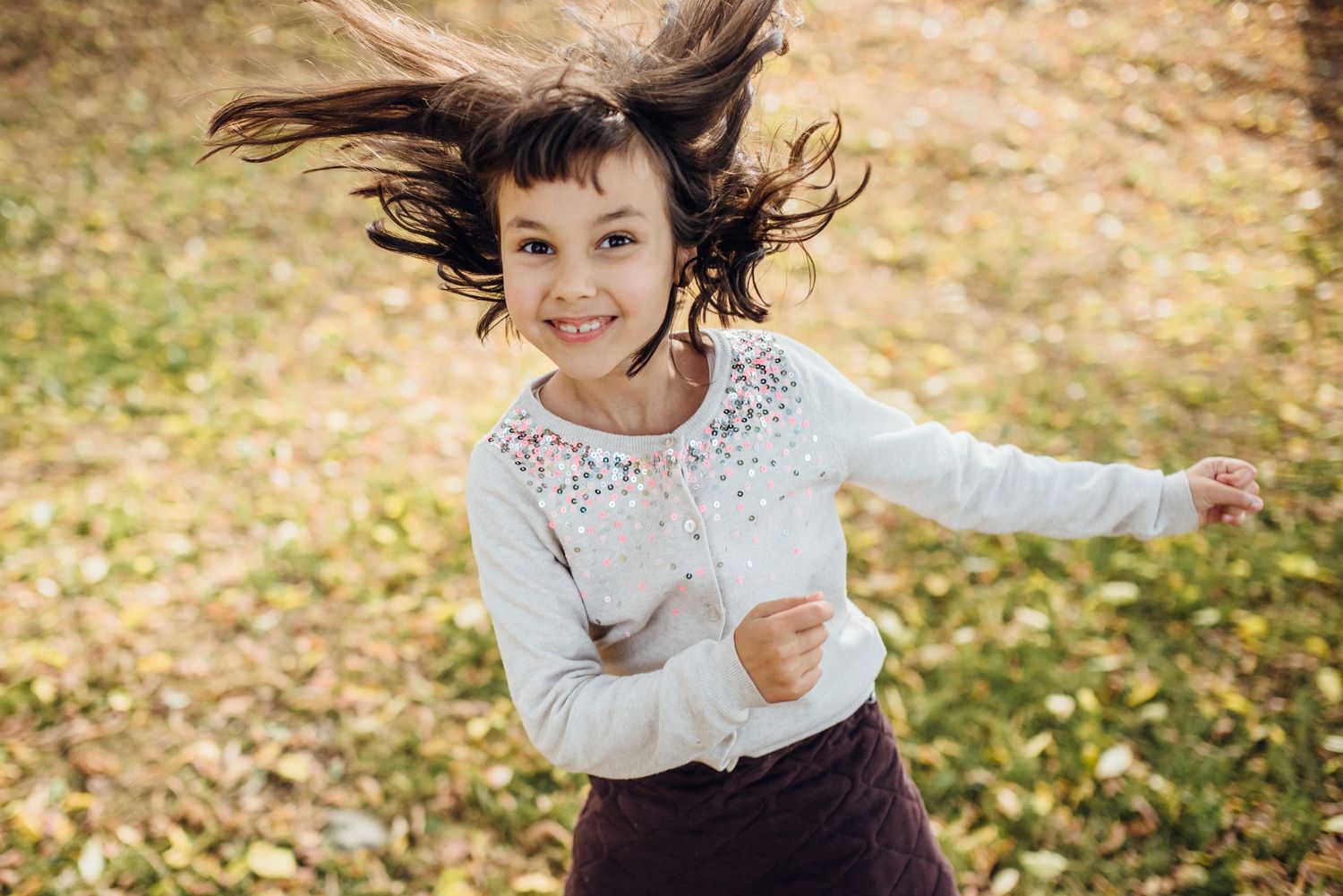 Child running and playing in autumn leaves during golden hour.