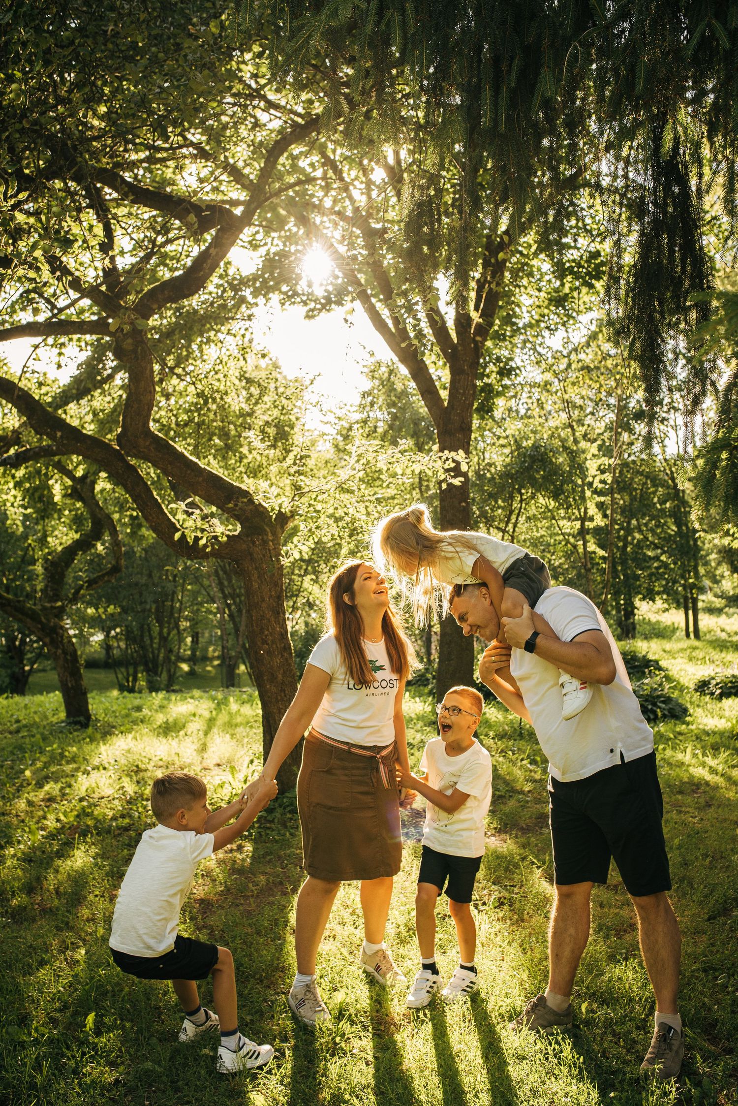Family photoshoot in a park during golden hour with sun flares through tree branches.