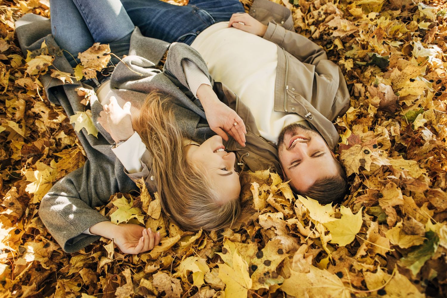 A couple lies together on fallen autumn leaves during a fall photoshoot.