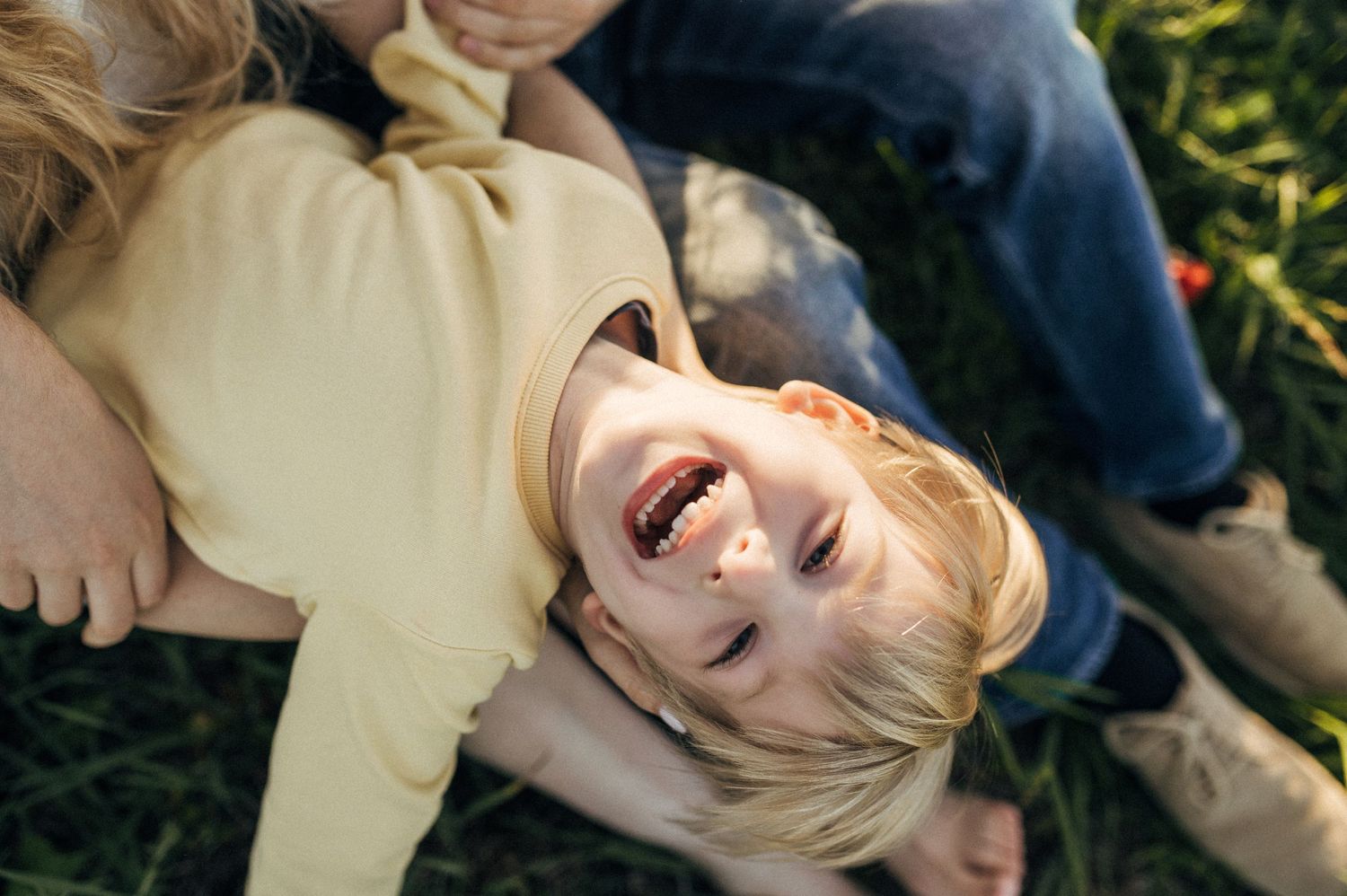 Family members sharing playful laughter while lying in grass during sunset.