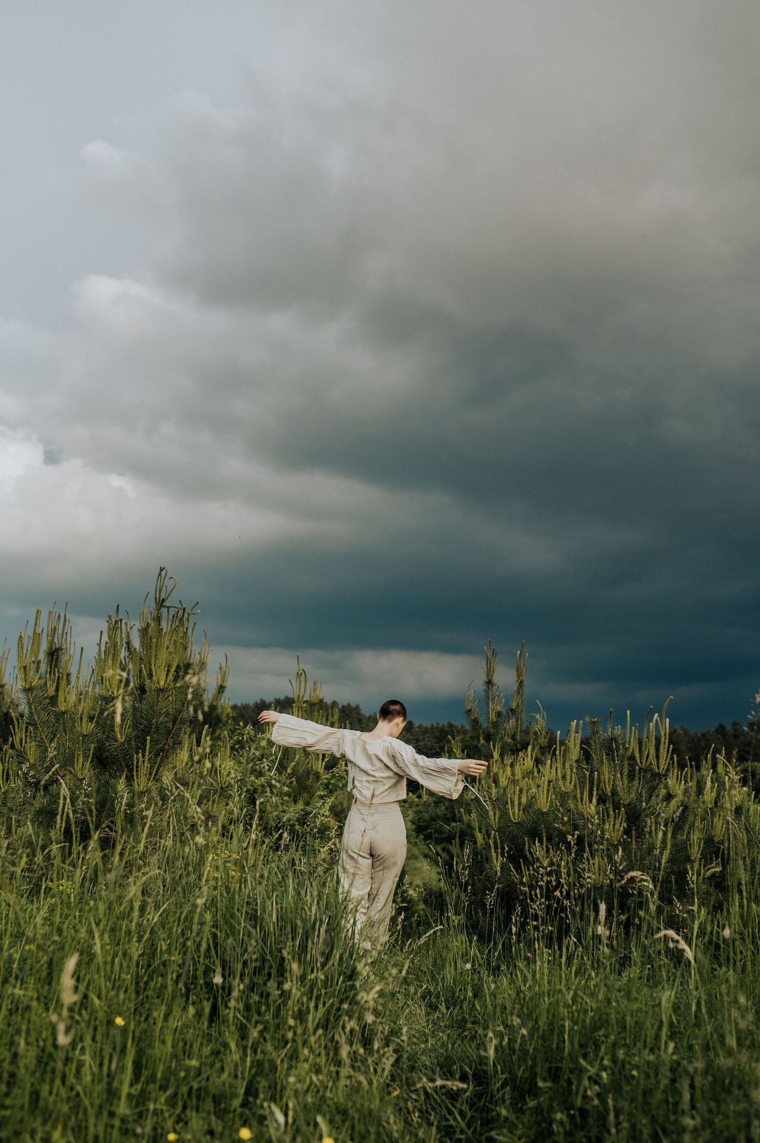 Figure in white clothing running through tall grass field under stormy sky.
