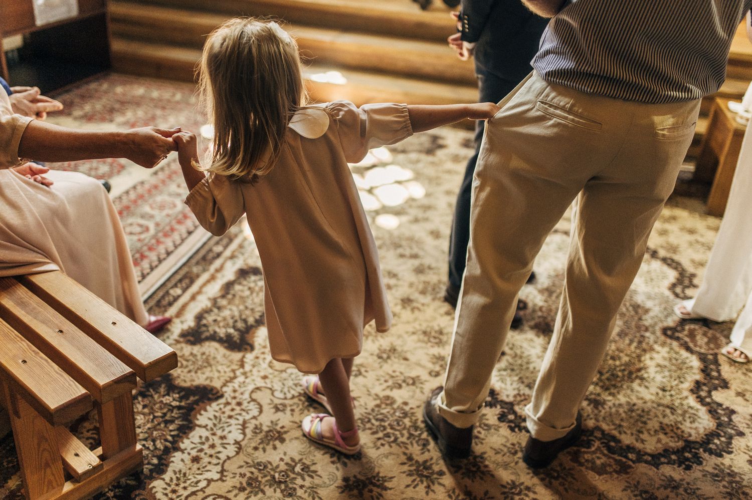 Little girl in pink dress holding hands with adults inside decorated church.