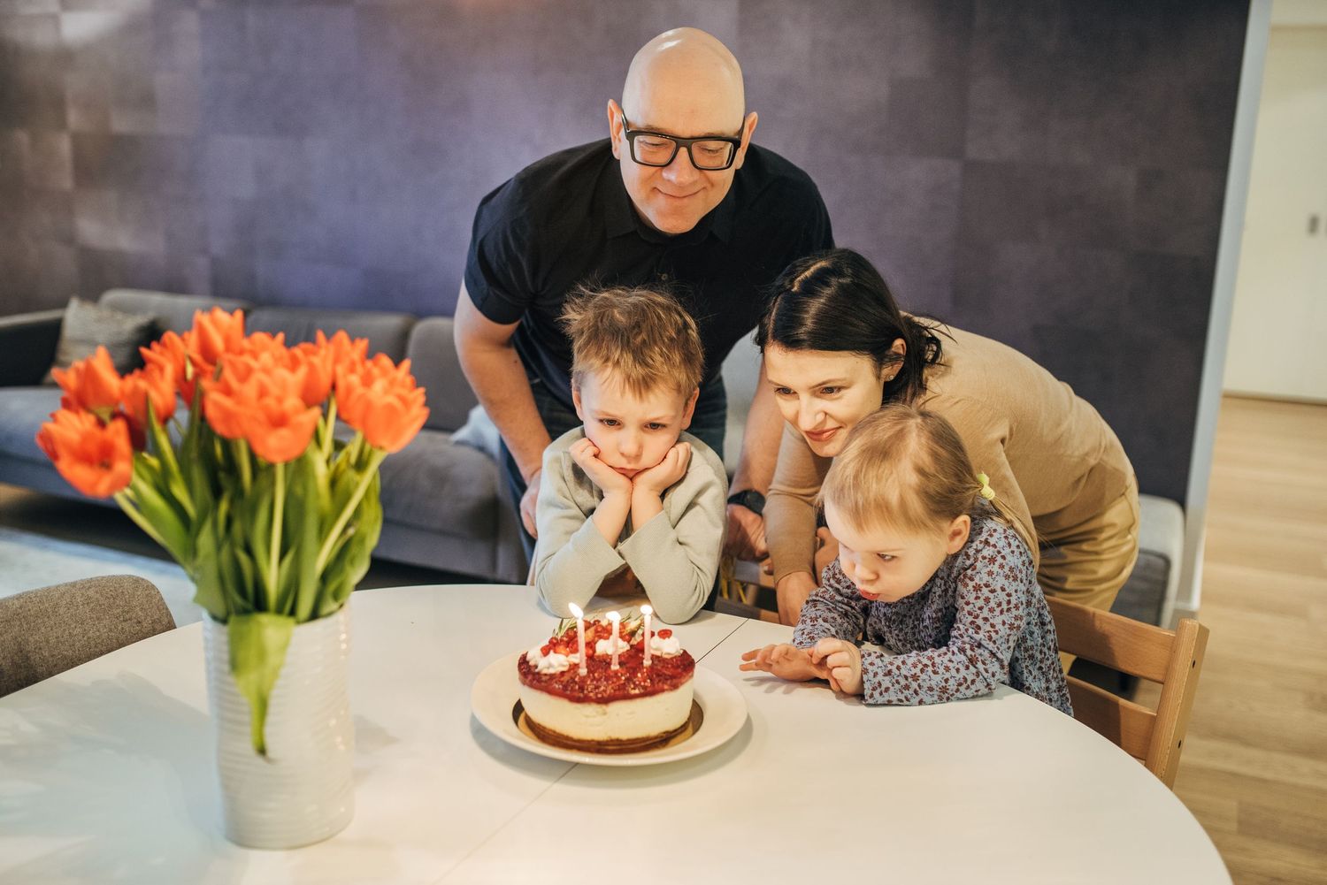 Birthday celebration with cake and orange tulips on dining table.