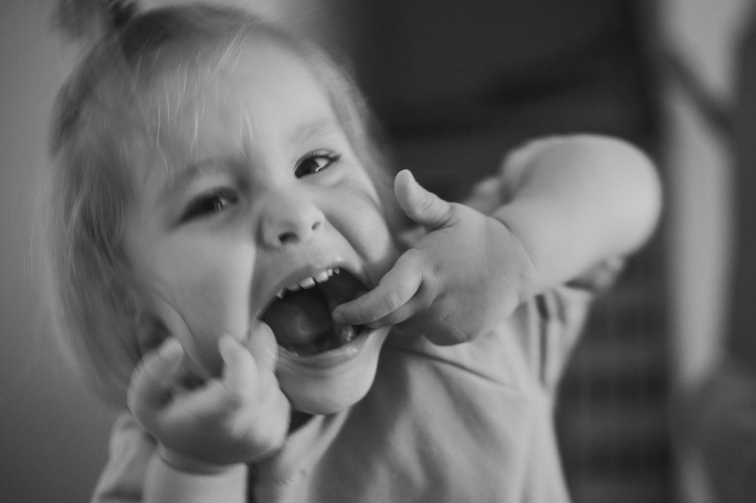 Black and white close-up of a joyful expression with hands framing face in playful pose.