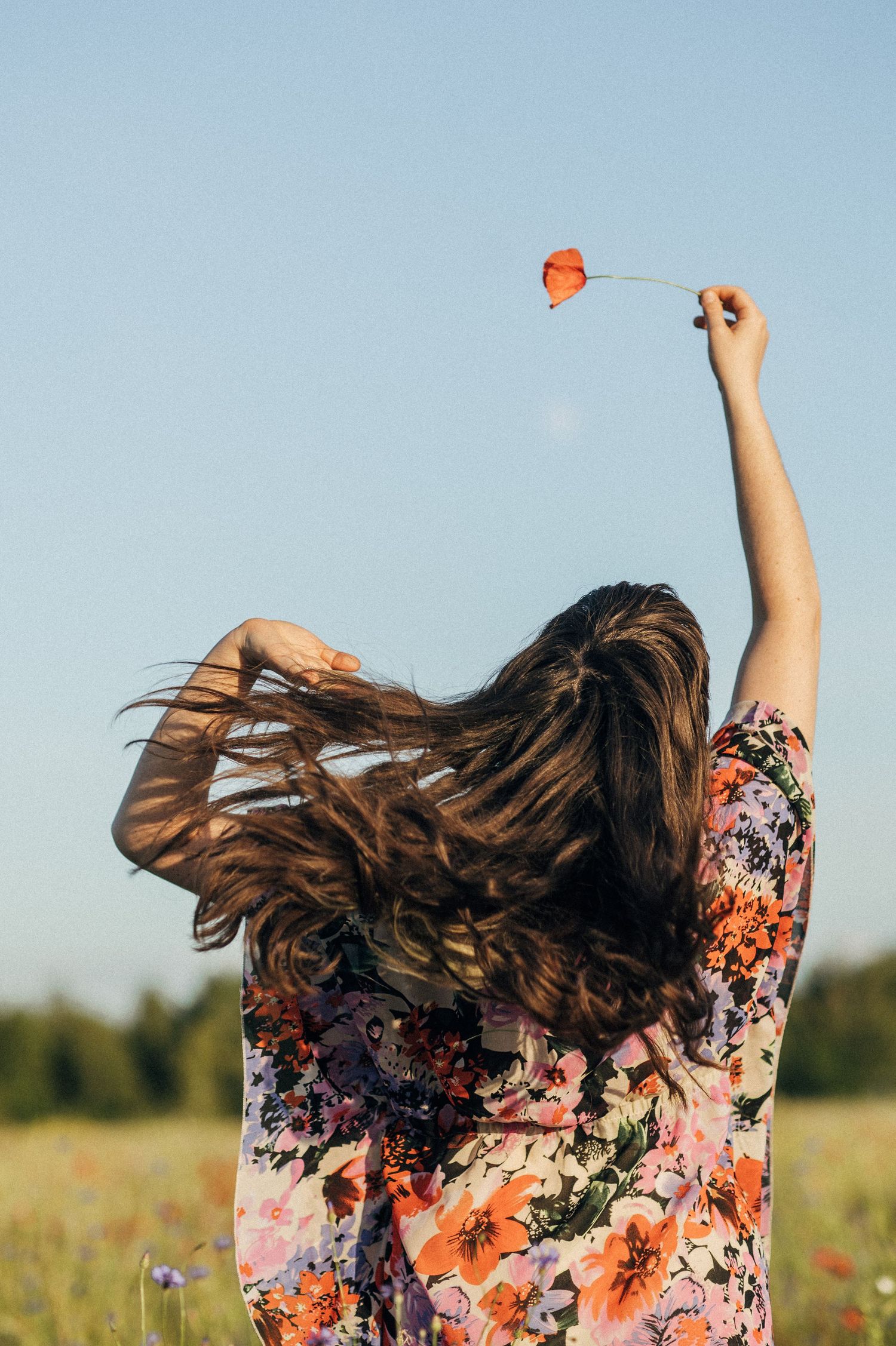 Hair flowing in the wind while dancing in a floral dress among wildflowers.