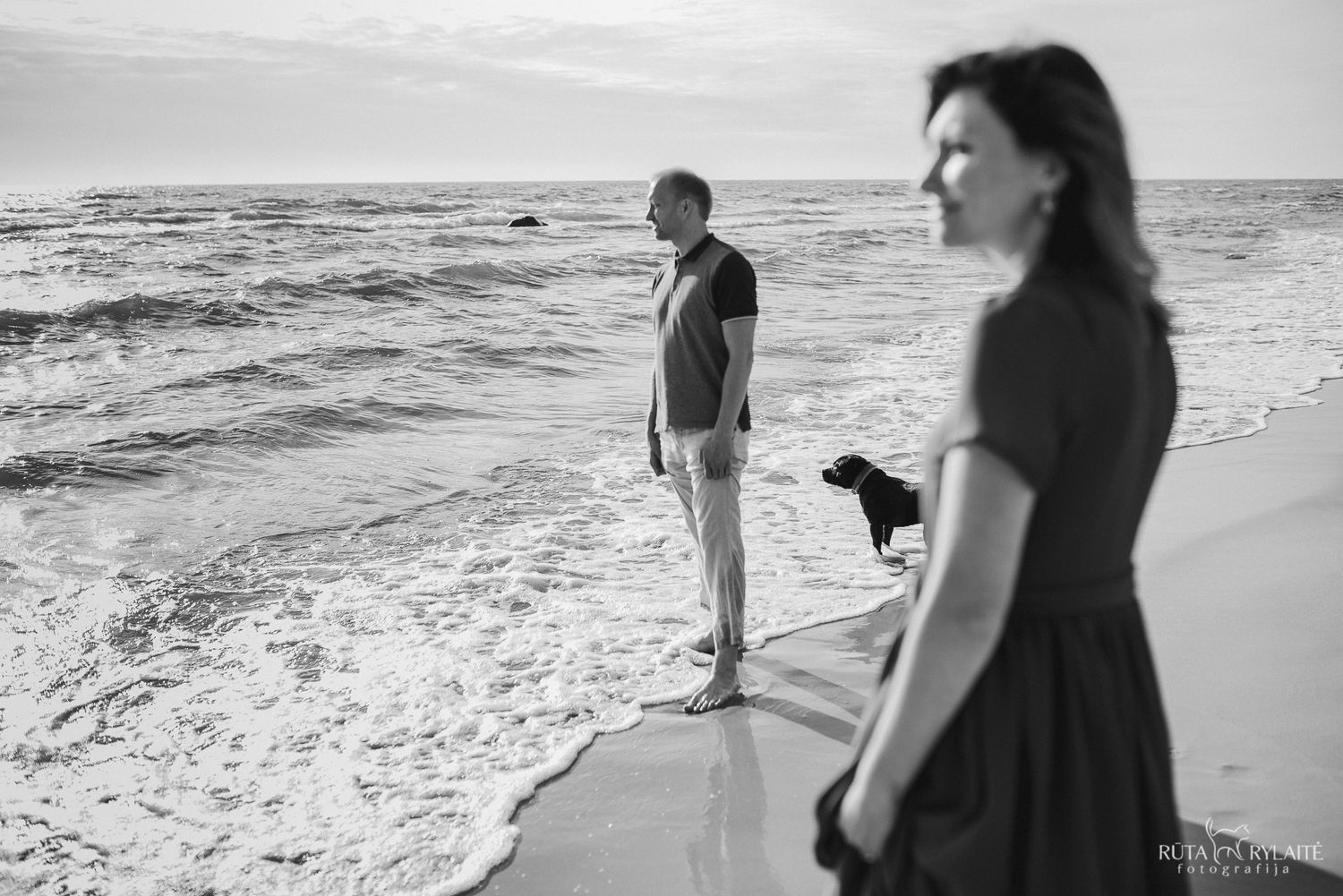 Black and white beach scene with people and waves along shoreline.