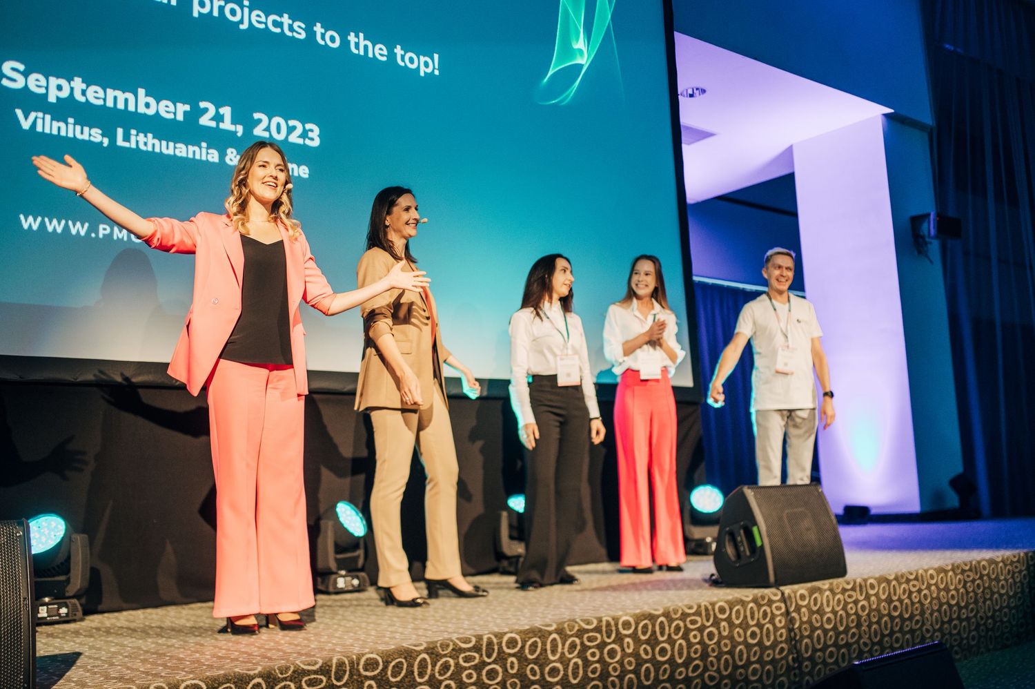 Conference stage with presenters lined up against blue and teal lighting backdrop.
