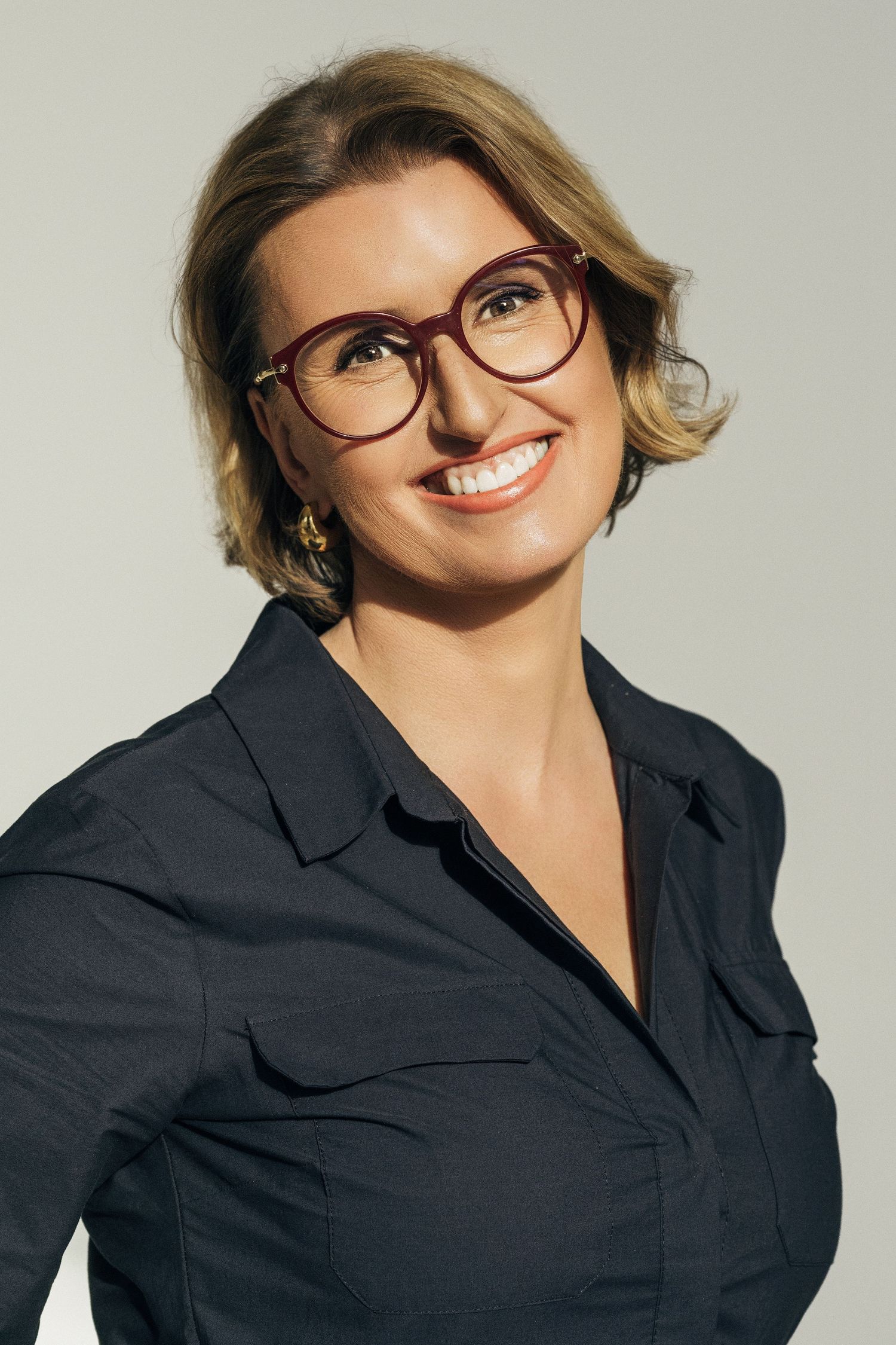 Professional headshot series of someone wearing glasses and a navy blazer smiling at different angles against a light background.