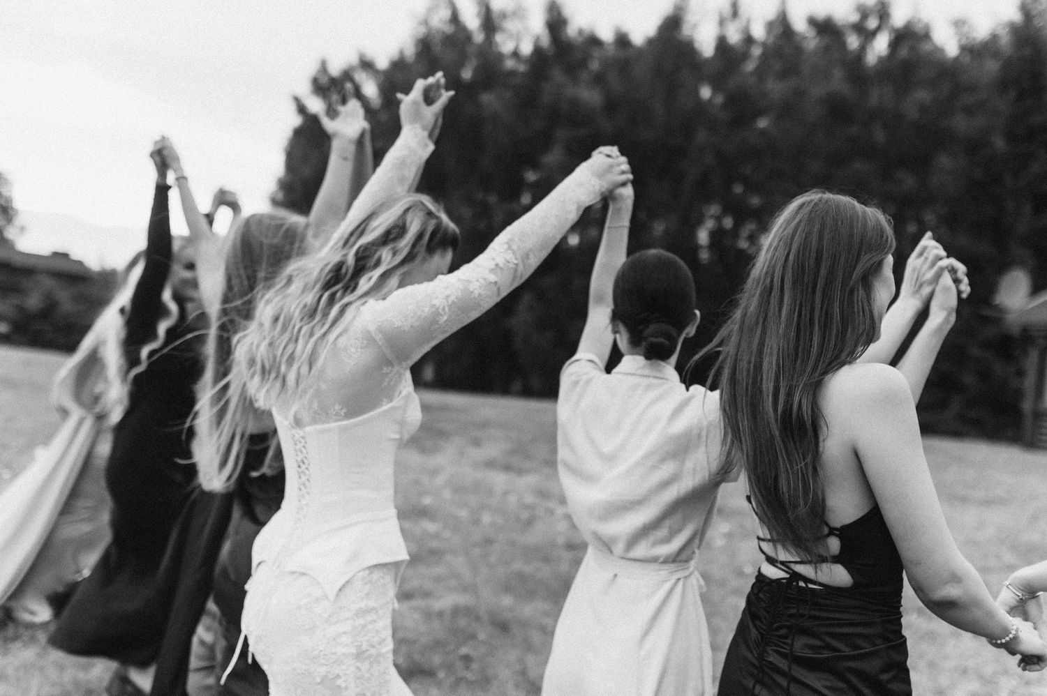 A group of people in formal attire dancing outdoors in a field with trees in the background.