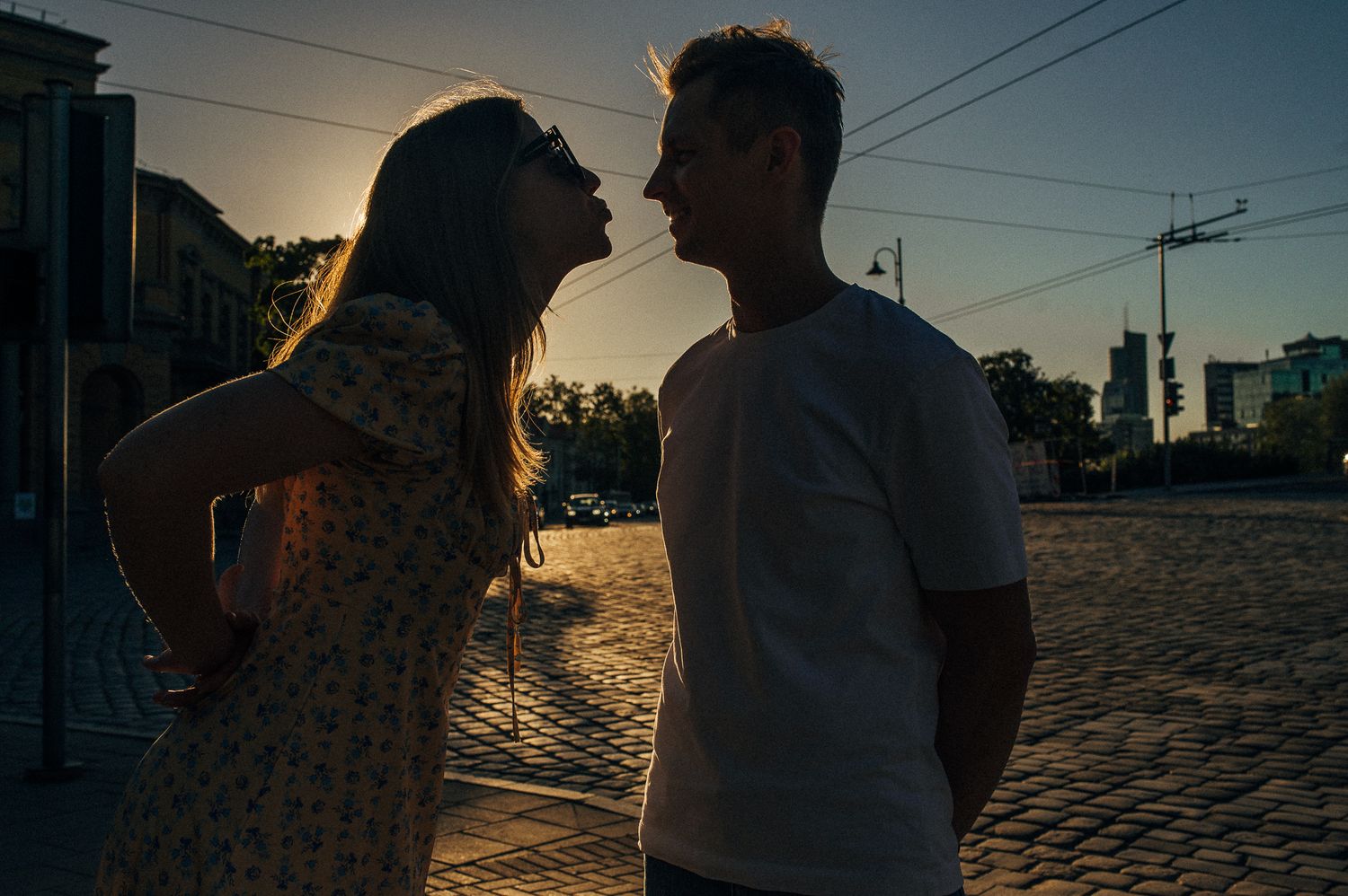 A romantic silhouette of a couple sharing an intimate moment at sunset on cobblestone streets.