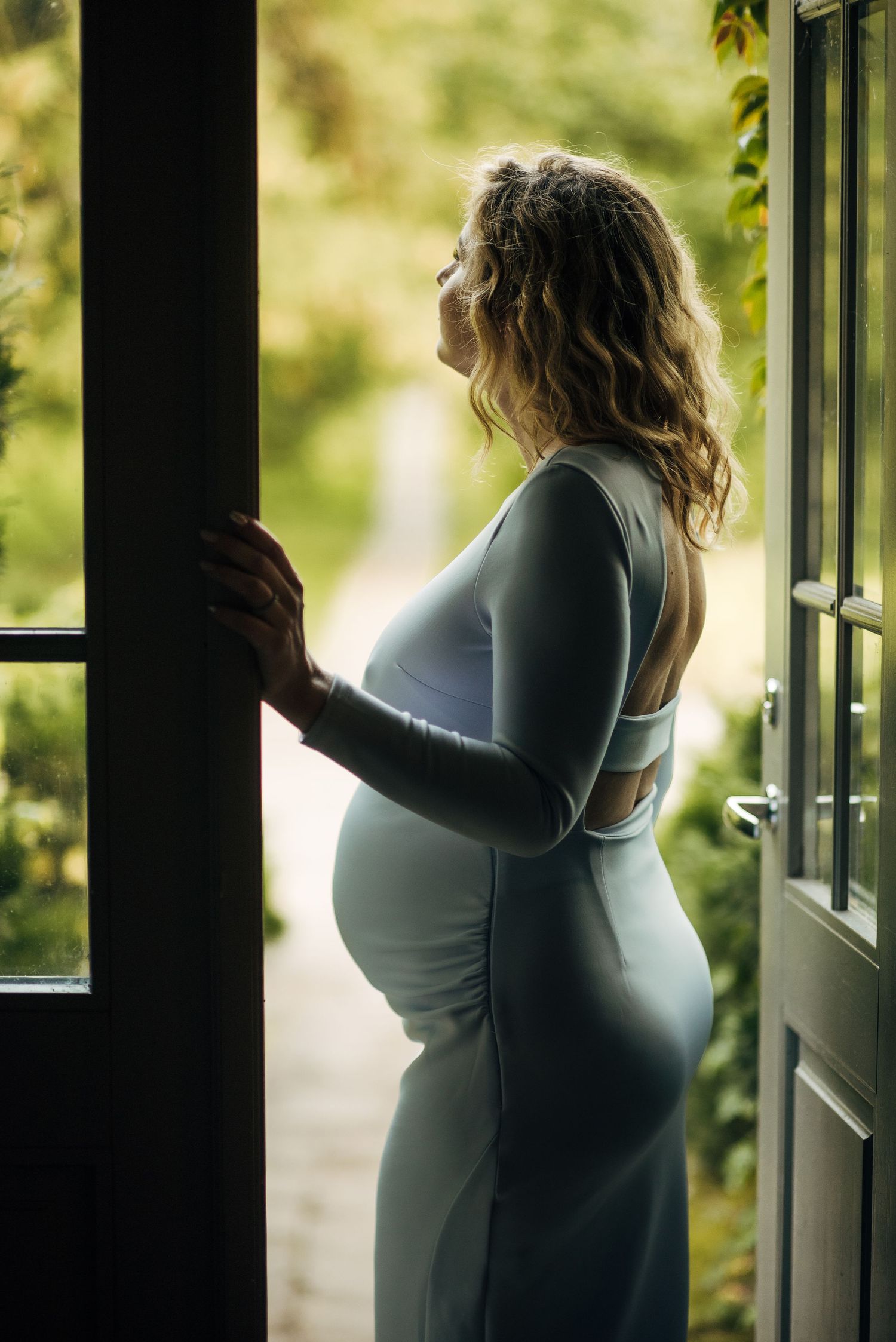 Silhouette of expecting mother by sunlit windows in an intimate moment.