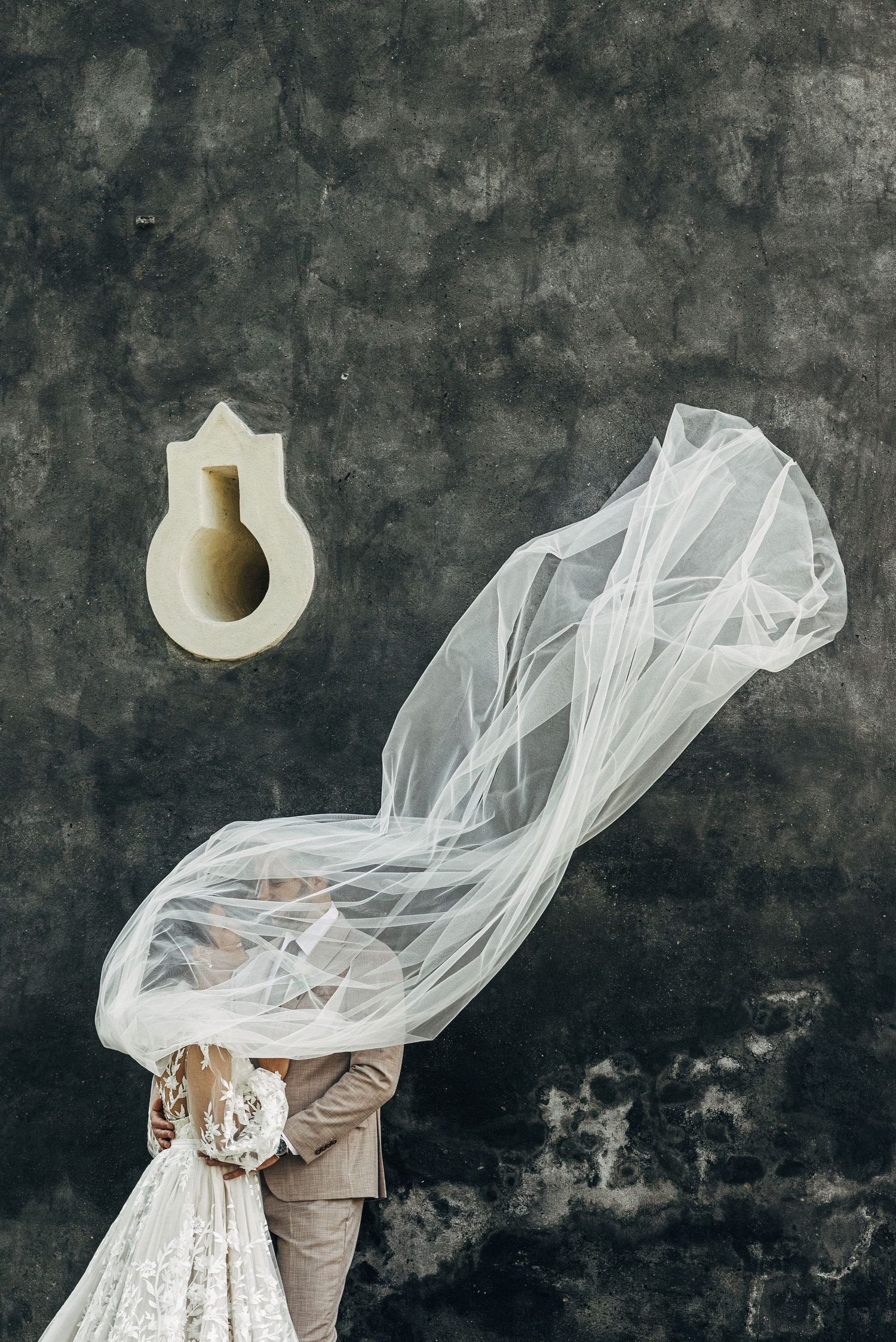 An artistic wedding photo showing flowing veil movement against a textured dark wall.