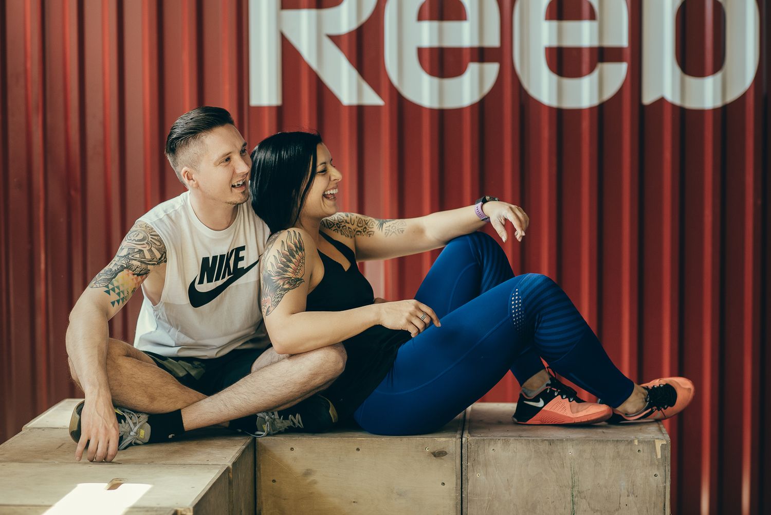 Athletes resting on wooden boxes in front of a red industrial wall.