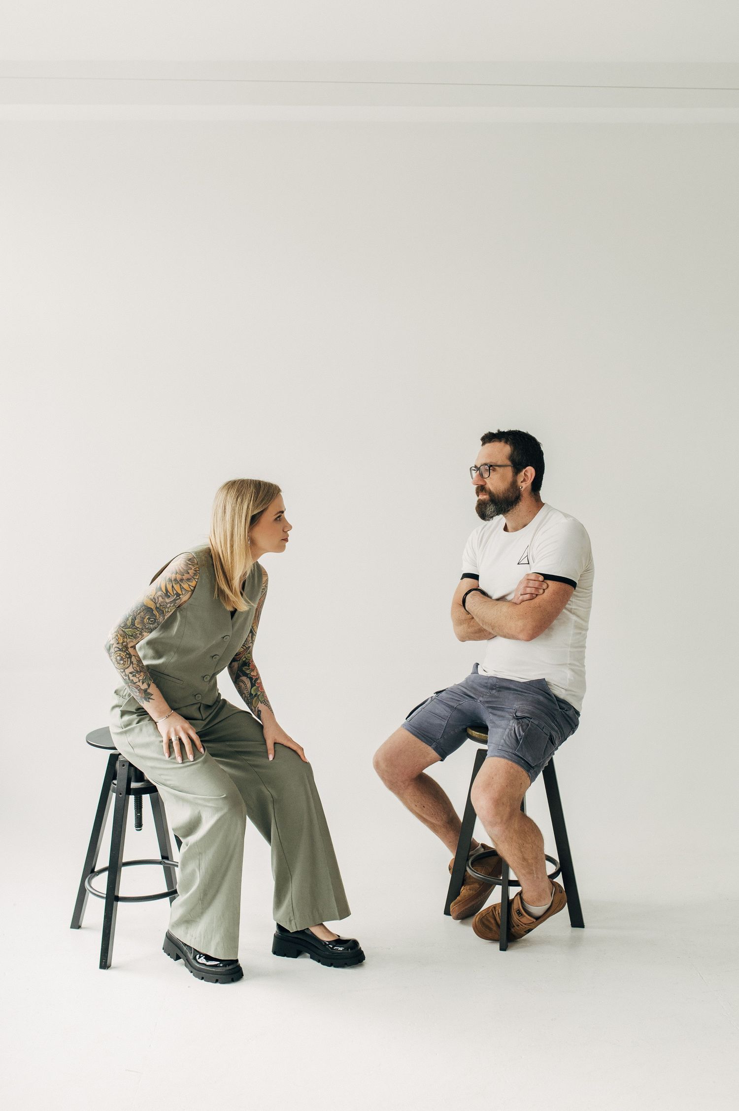 Two people sitting on stools engaged in animated conversation against a white background.