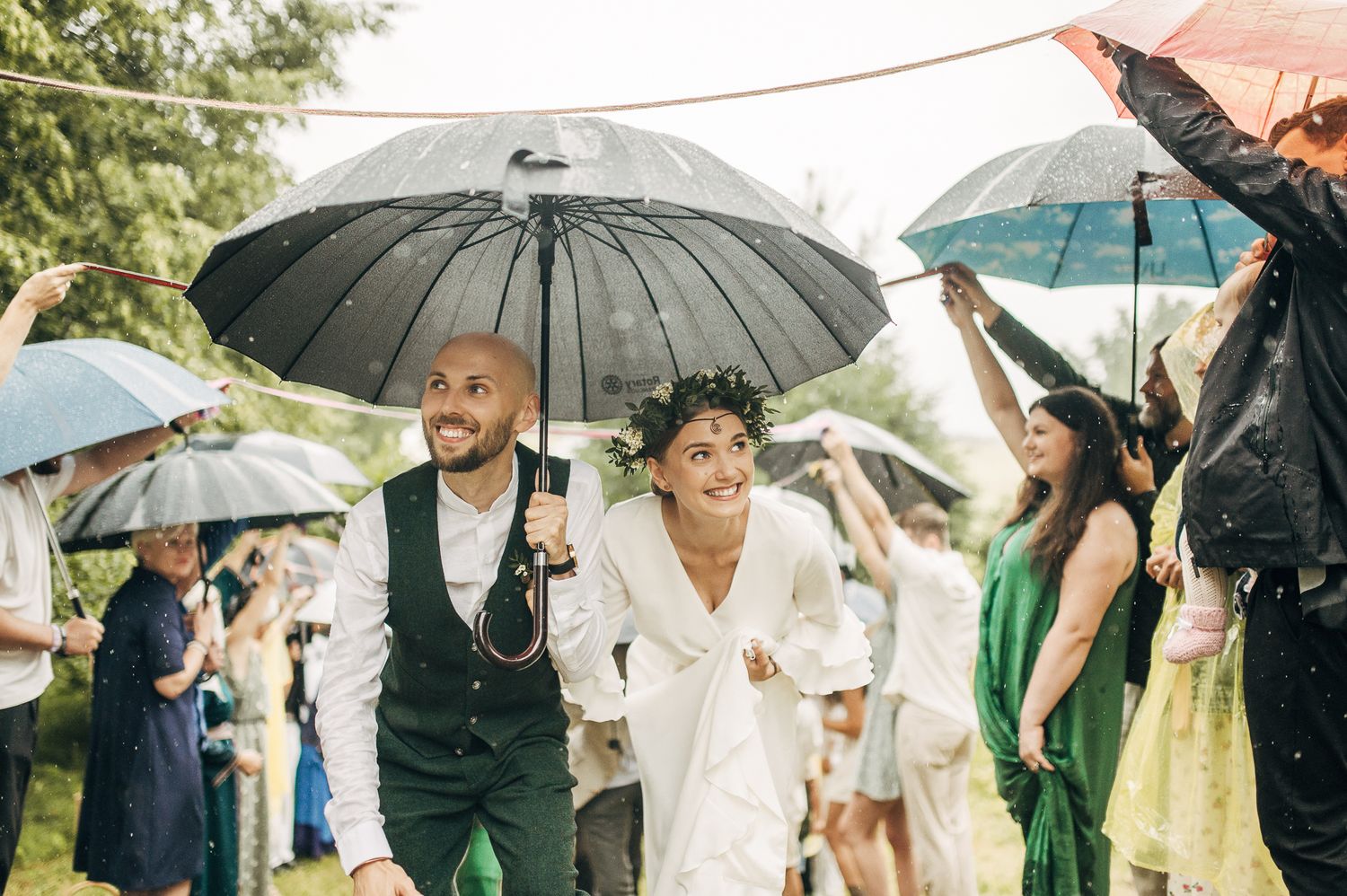 Wedding party walks under umbrellas during a joyful rainy celebration.
