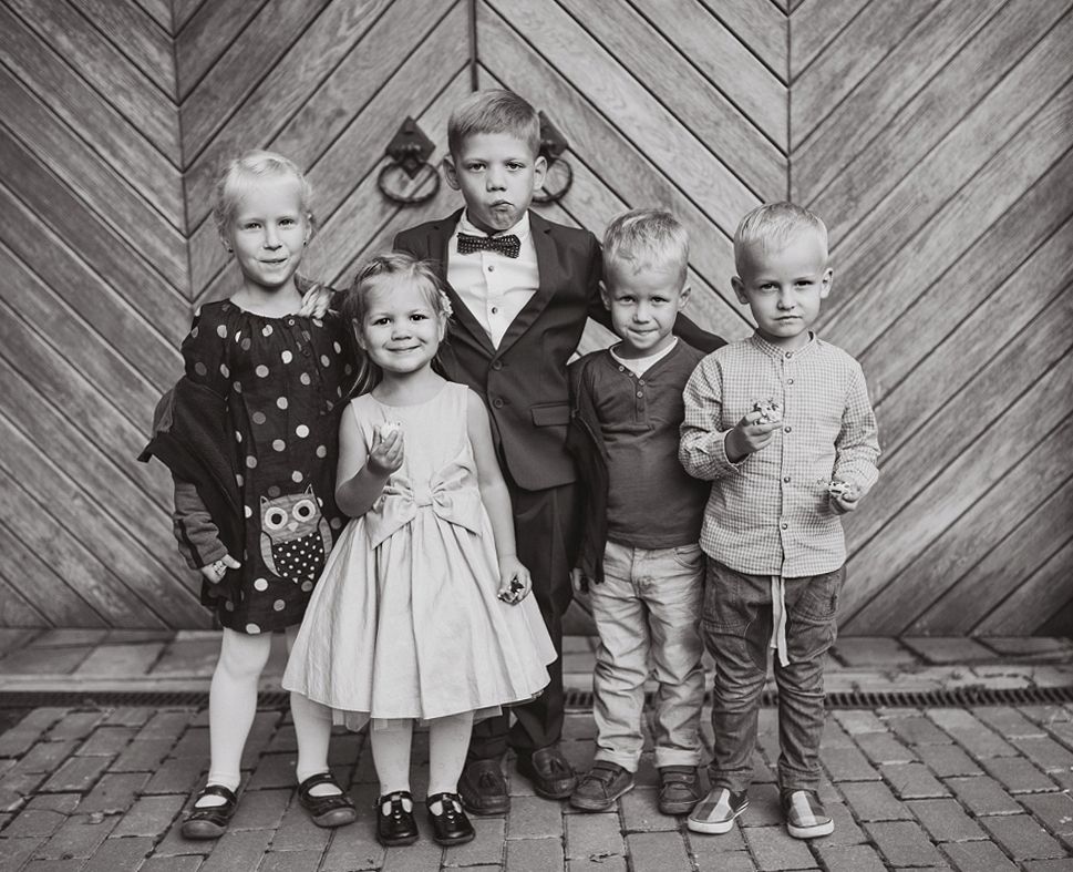 Black and white photo of children lined up against a wooden chevron wall pattern.