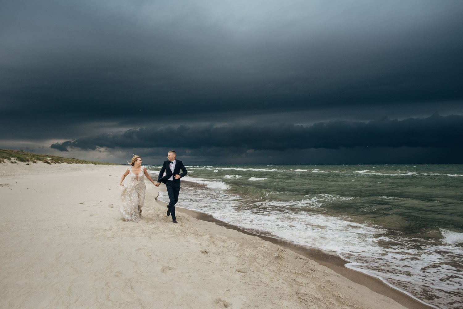 Wedding couple embracing on a stormy beach with dramatic dark clouds overhead.