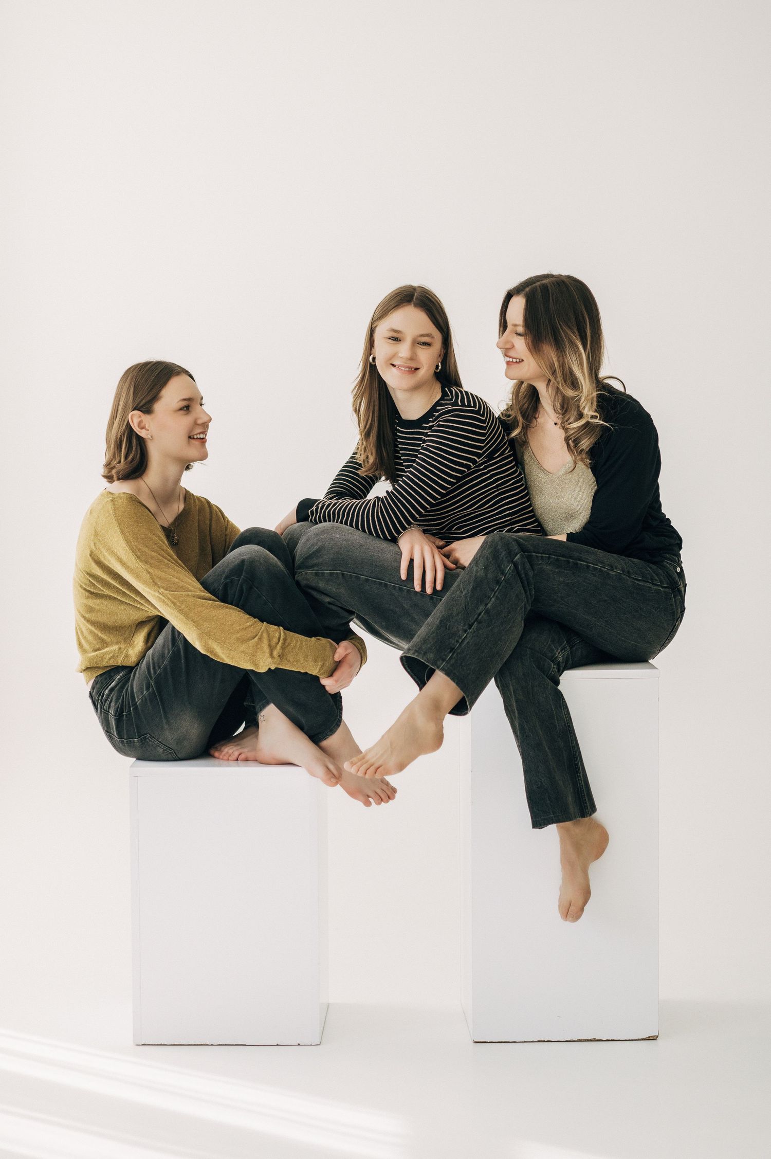 Friends in casual outfits sit playfully on white blocks in a minimalist studio setting.