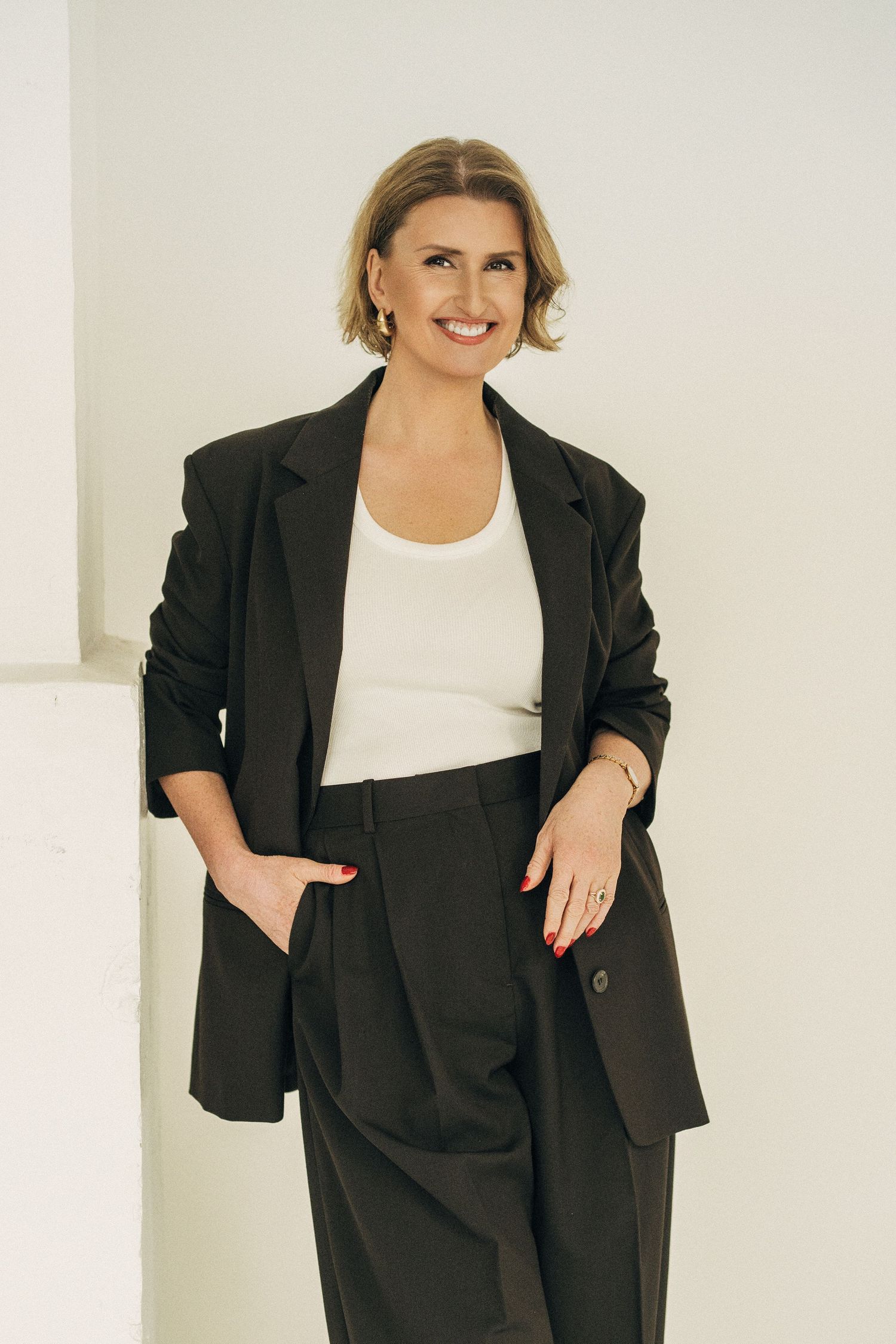 A person poses in a black blazer and white top against a white background in a fashion photoshoot series.