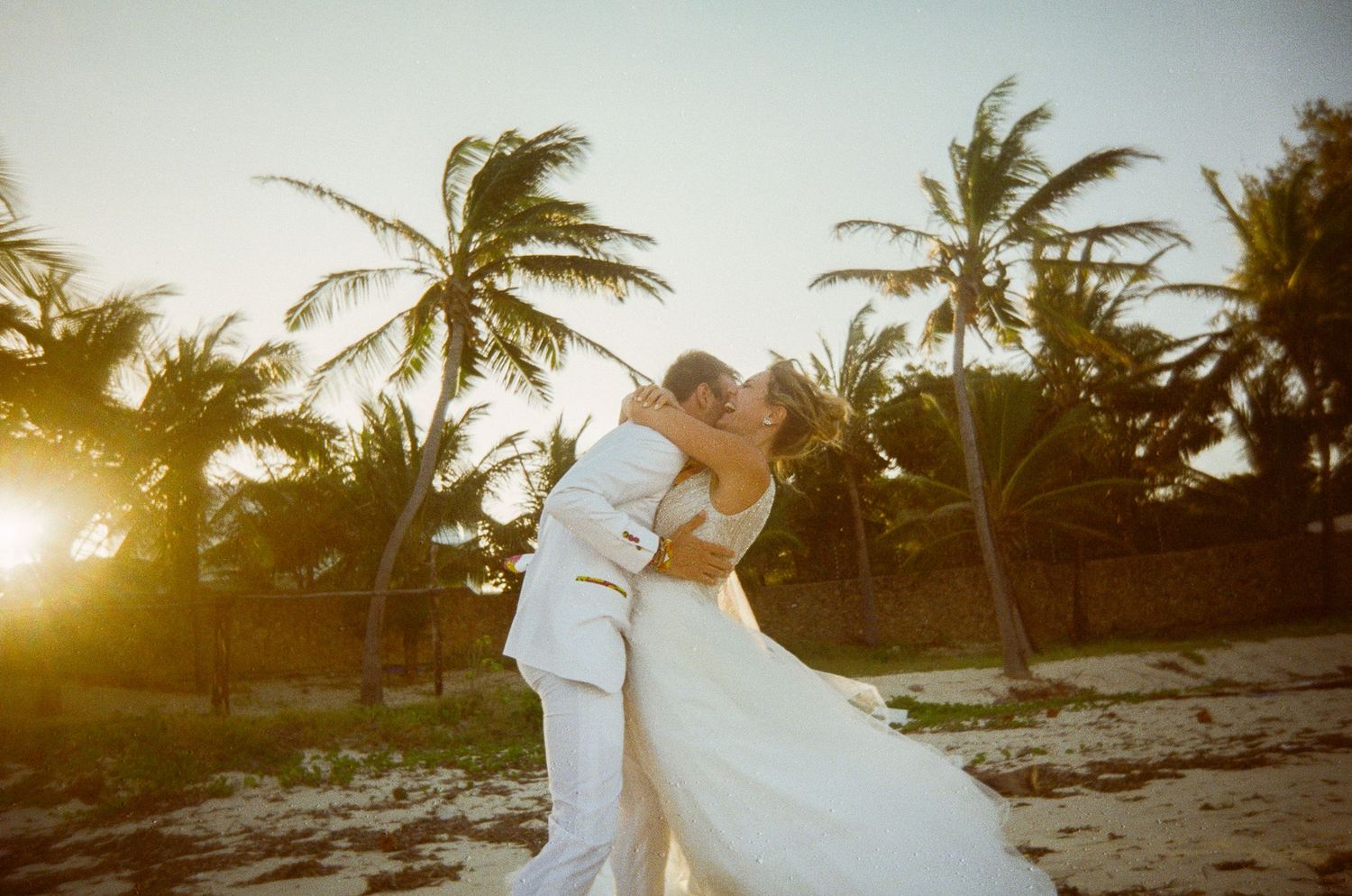 Romantic beach wedding scene with palm trees silhouetted against golden sunset.