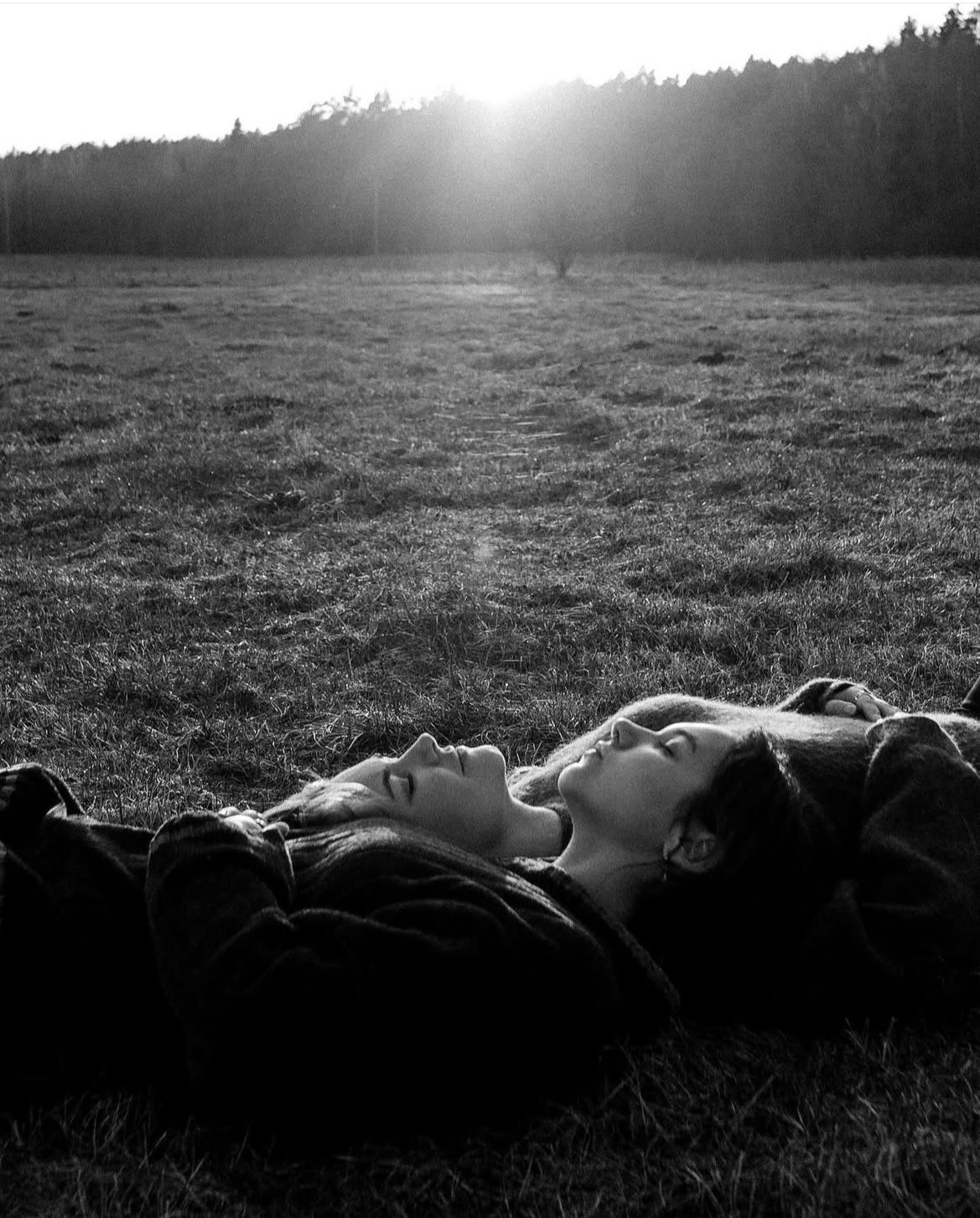 Black and white silhouette of people lying in grass during sunset.