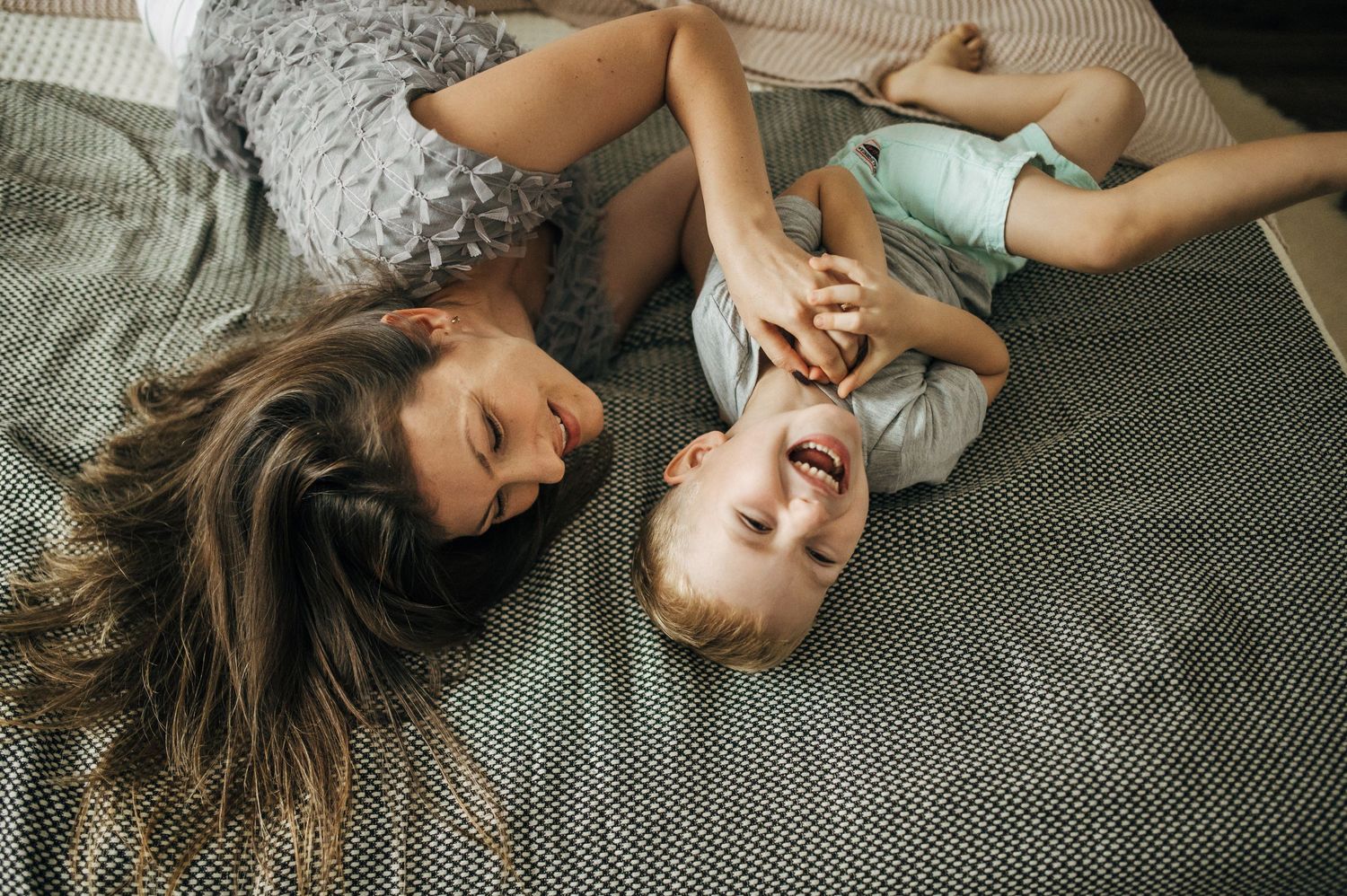 Two siblings lying on a knitted rug while playing and laughing together.
