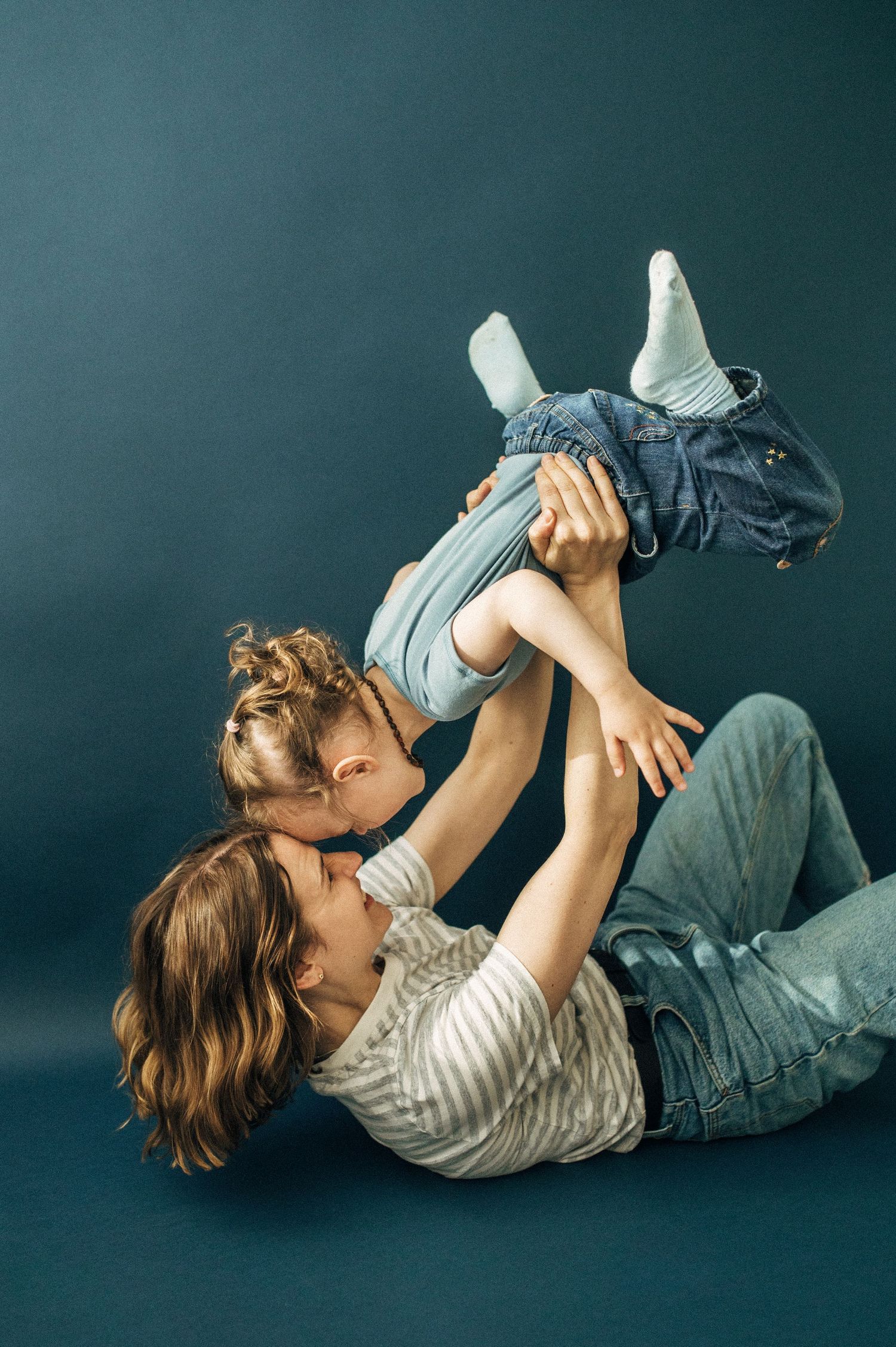 A playful series of photos showing someone lying on their back holding up a young child in a blue shirt against a dark background.