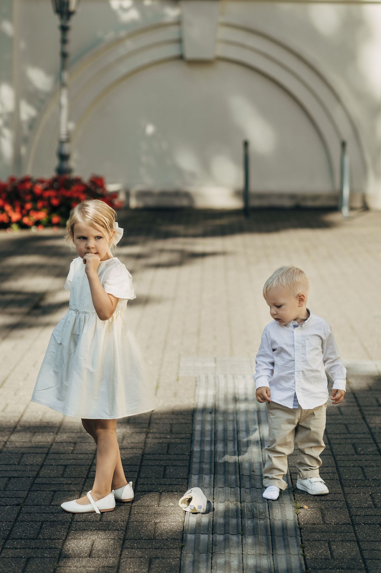 Two young children in white formal outfits standing on a paved outdoor area.