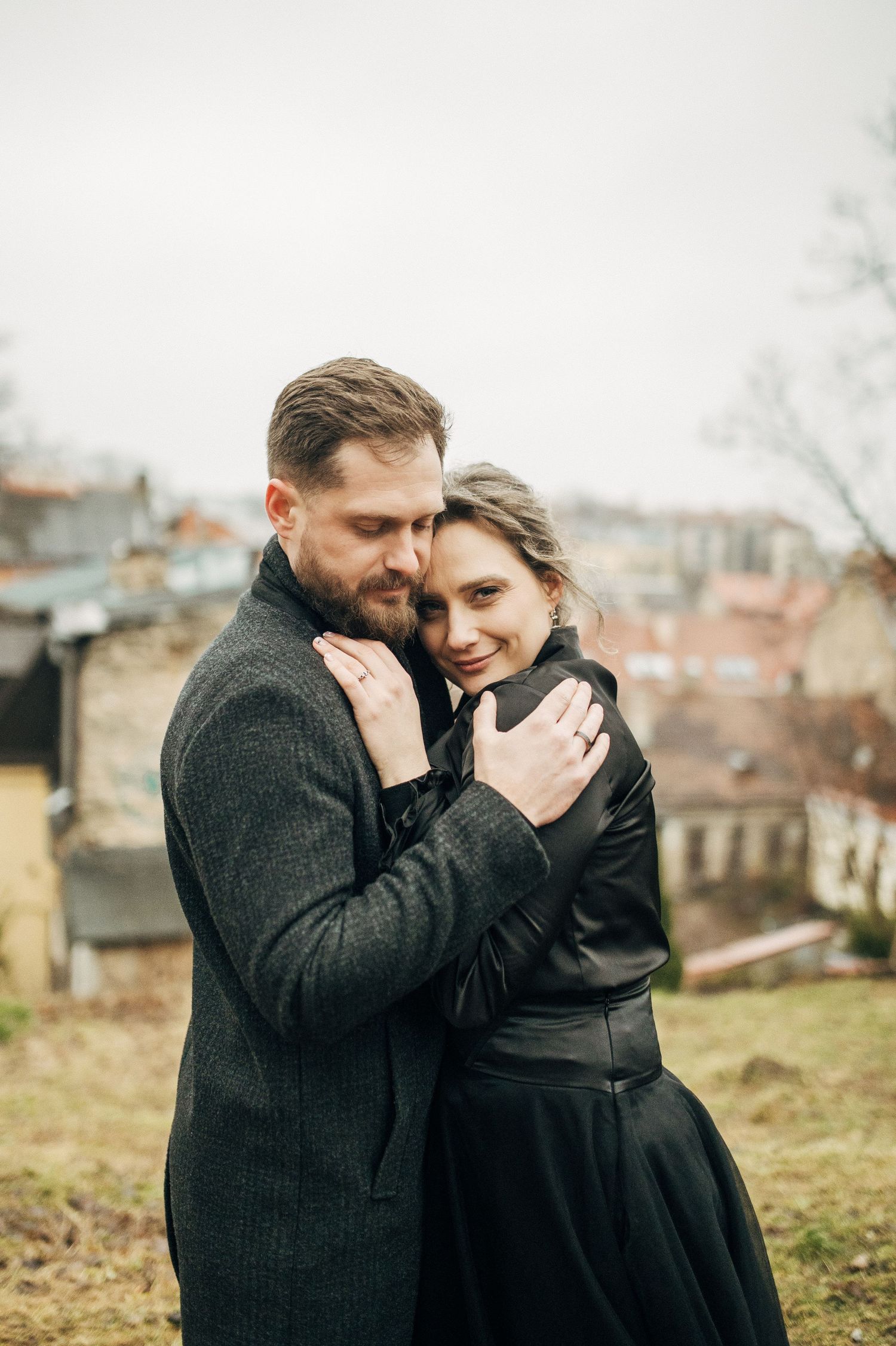 Intimate moment shared between couple on hillside with city view.
