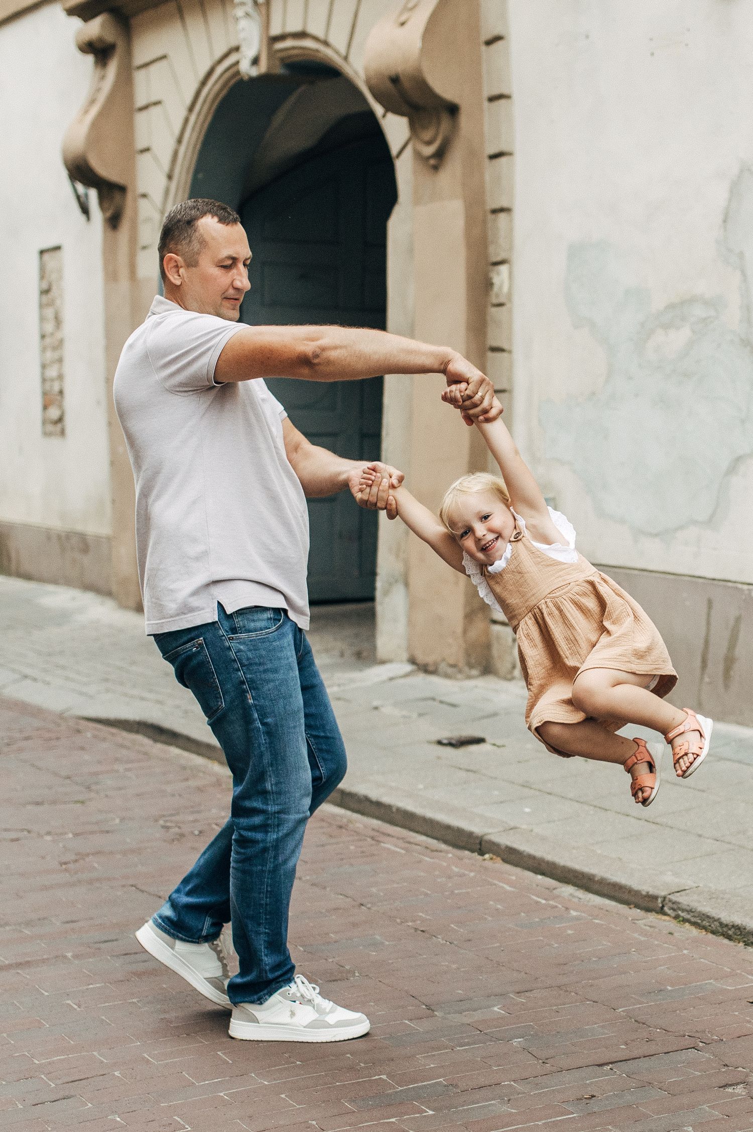 Sequence showing playful spinning motion on a cobblestone street beside stone architecture.