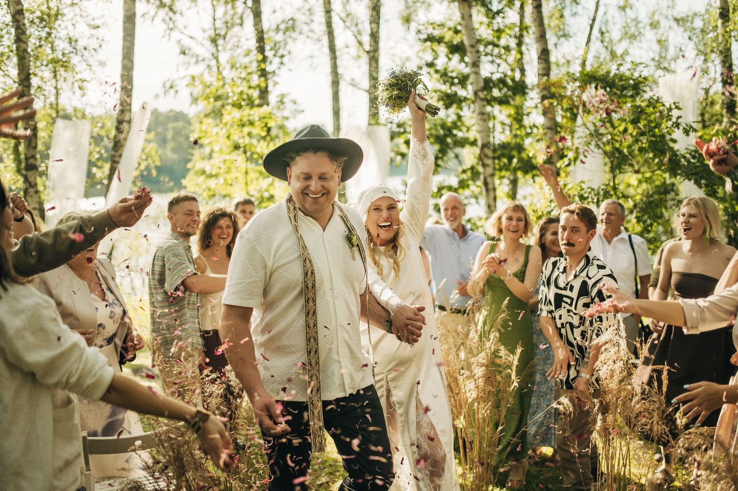 Wedding guests celebrate and dance together in a sunlit outdoor garden setting during a joyful reception.