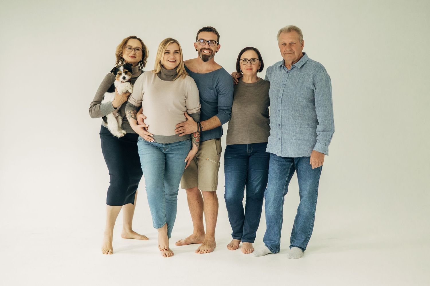 Three people in casual clothes share tender embraces and laughter against a light studio backdrop.