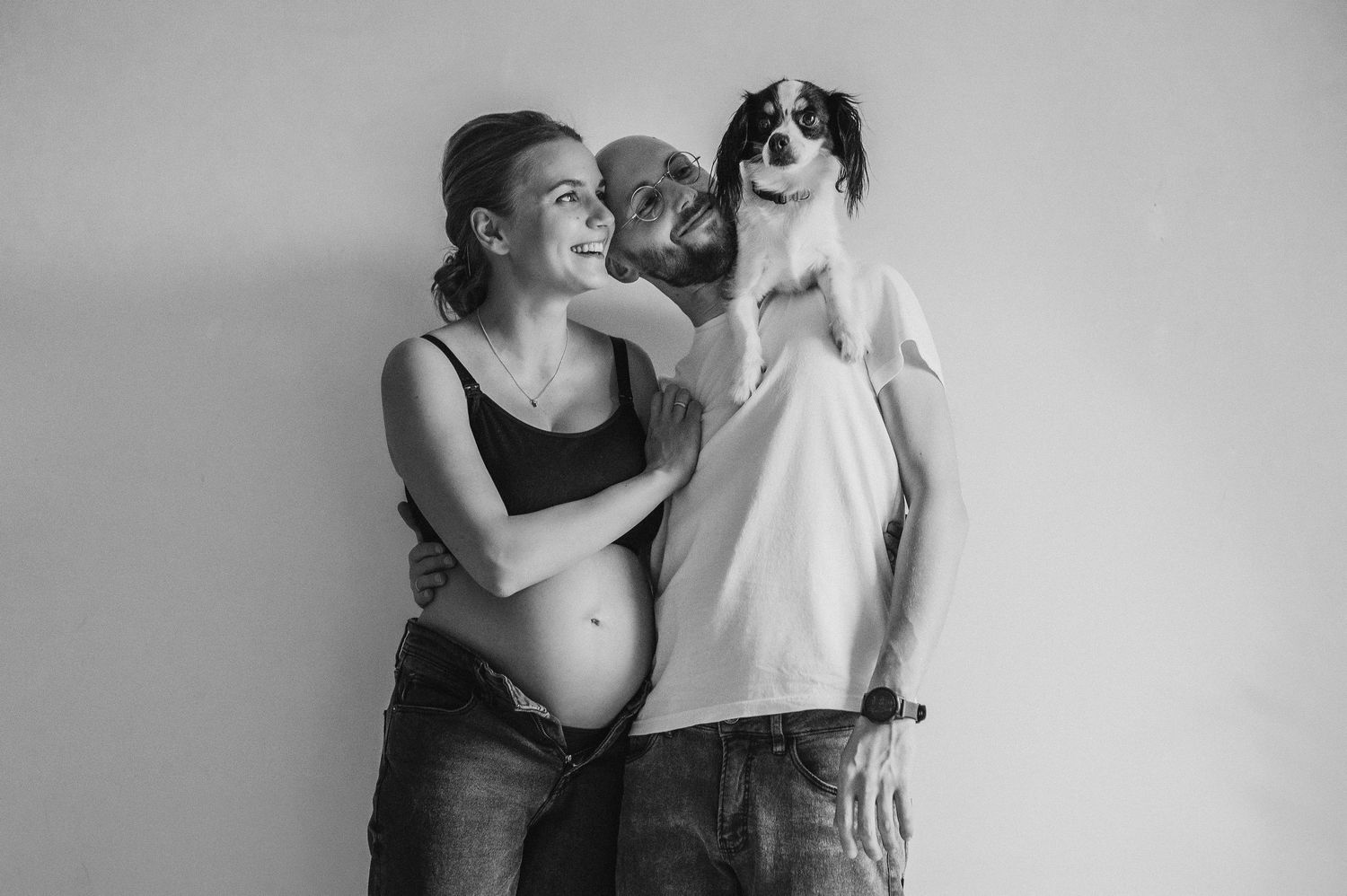 A black and white portrait of an expecting couple with their cat.