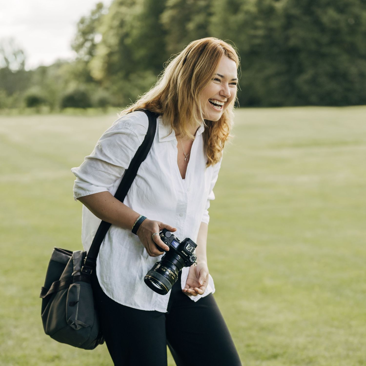 Professional photographer with camera equipment laughing in a sunny green field.