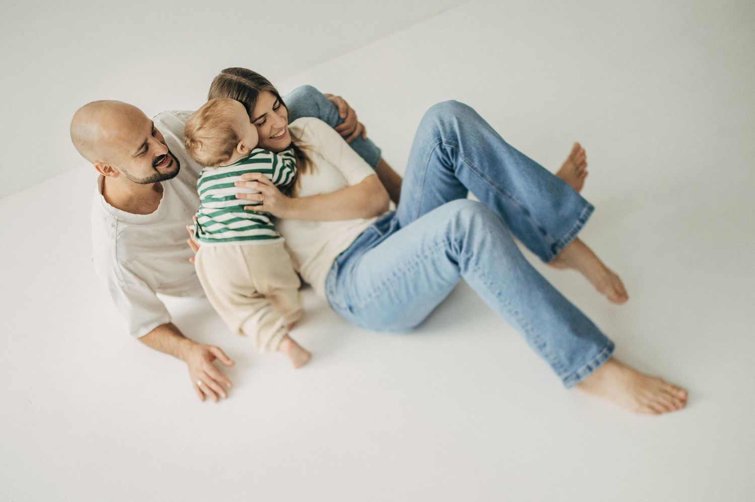 Baby lying on white blanket in casual outfit during lifestyle photography session.