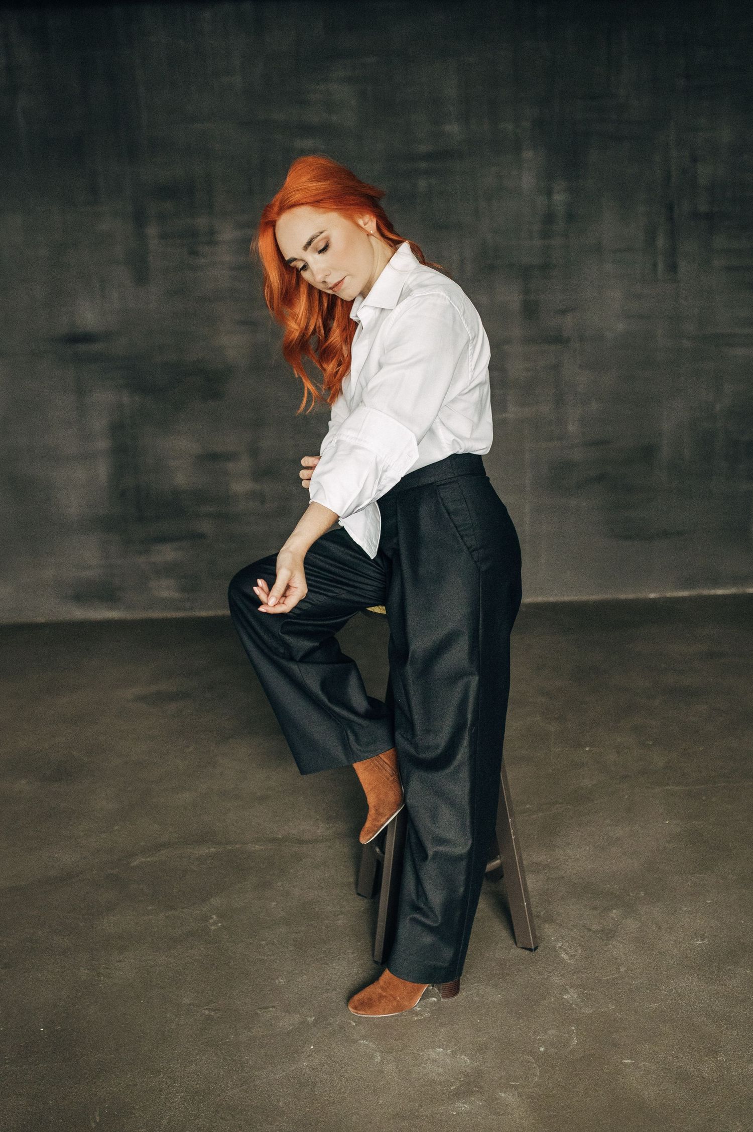 Fashion portrait of person in white top and dark pants crouching on concrete floor.