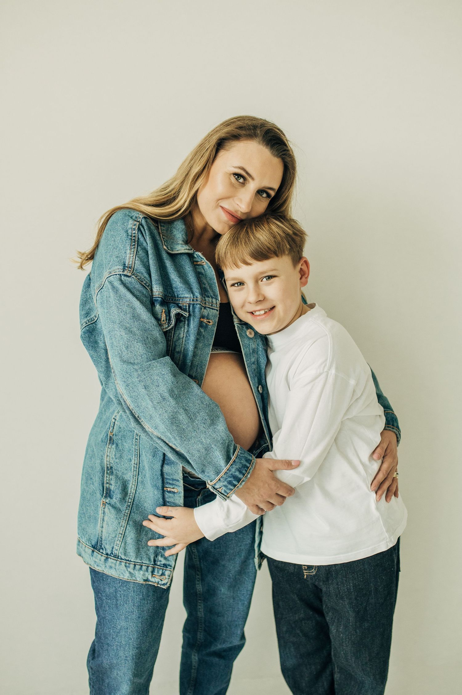 Mother and child embracing in casual denim outfits against neutral background.