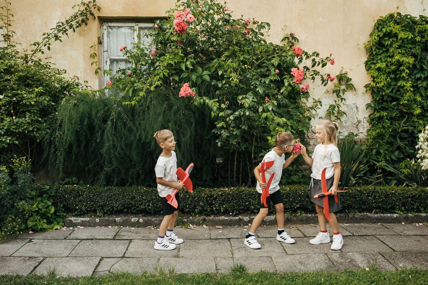 Sequence showing children in white sneakers walking along a garden path with blooming roses.