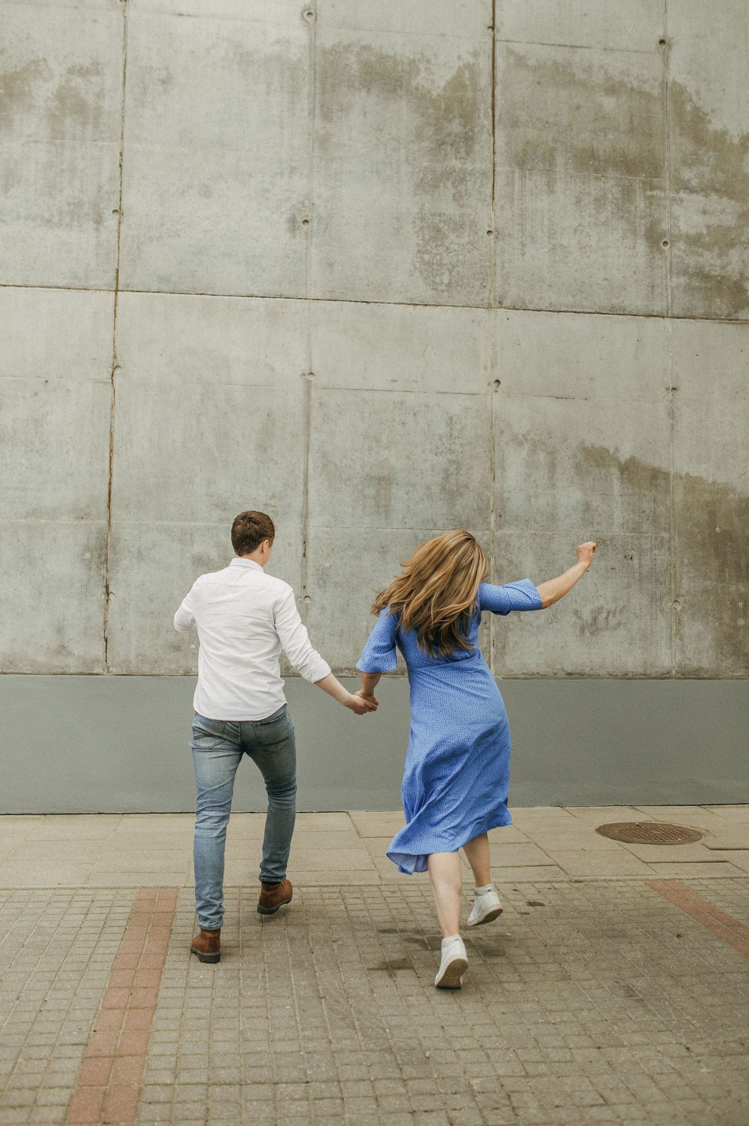 Two people dance playfully along a concrete wall and brick pathway.