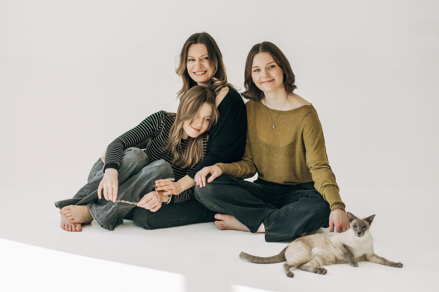Studio lifestyle portraits with two people and cat relaxing on white floor.