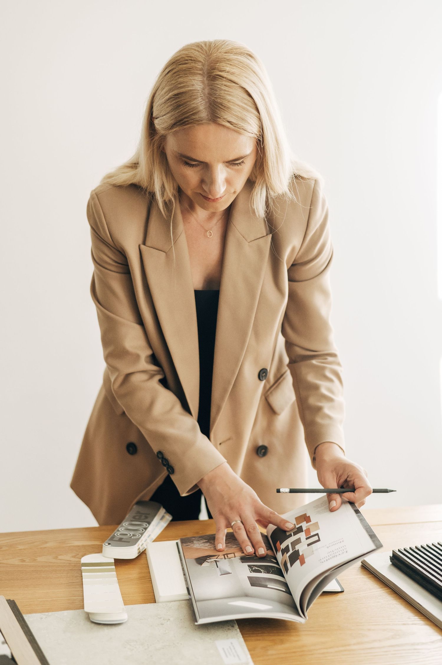 Interior designer in tan blazer reviewing samples from catalog at desk.