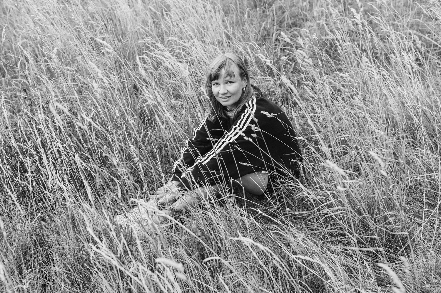 A figure in dark clothing walking through tall grass in a black and white photograph.