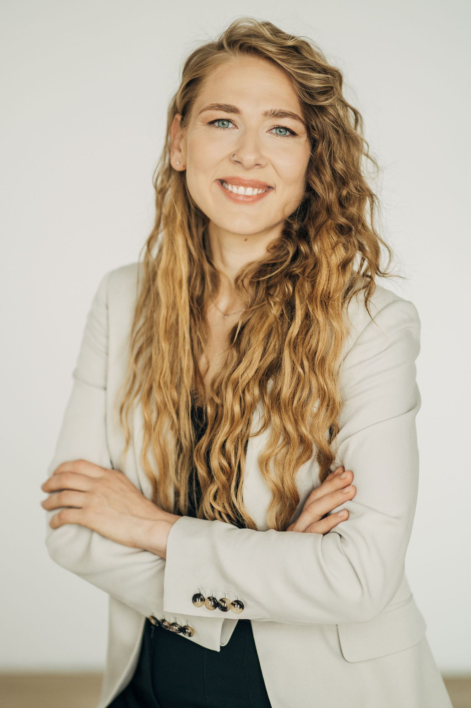 Person in cream blazer poses against white background with wavy blonde hair and natural smile.