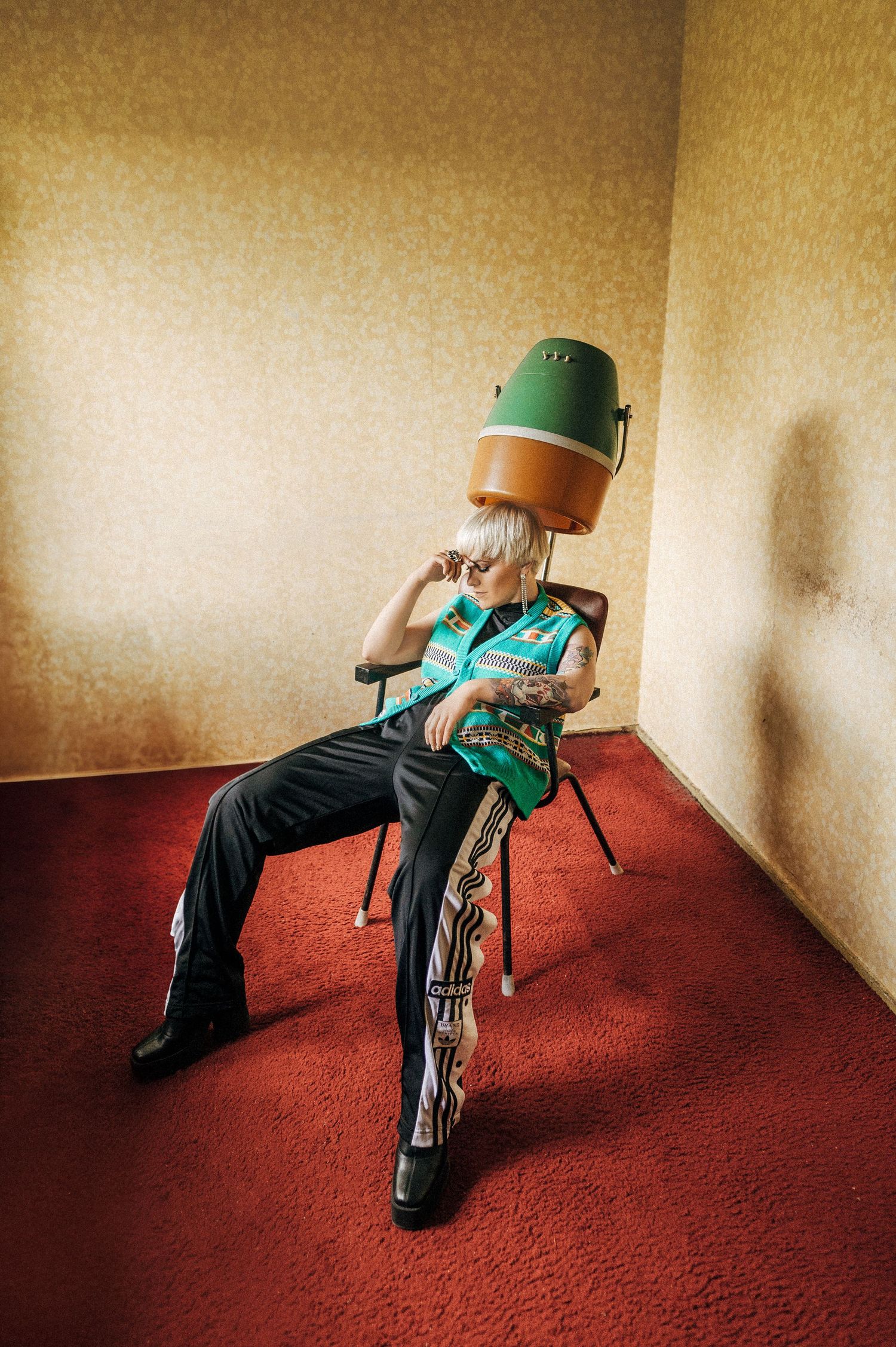 A surreal portrait of someone sitting in a chair with a beauty salon hair dryer on their head in a red carpeted room.