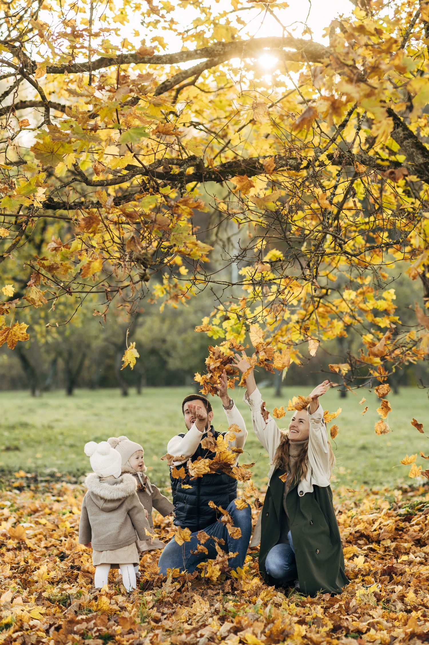 Family gathering under golden autumn trees with fallen leaves.