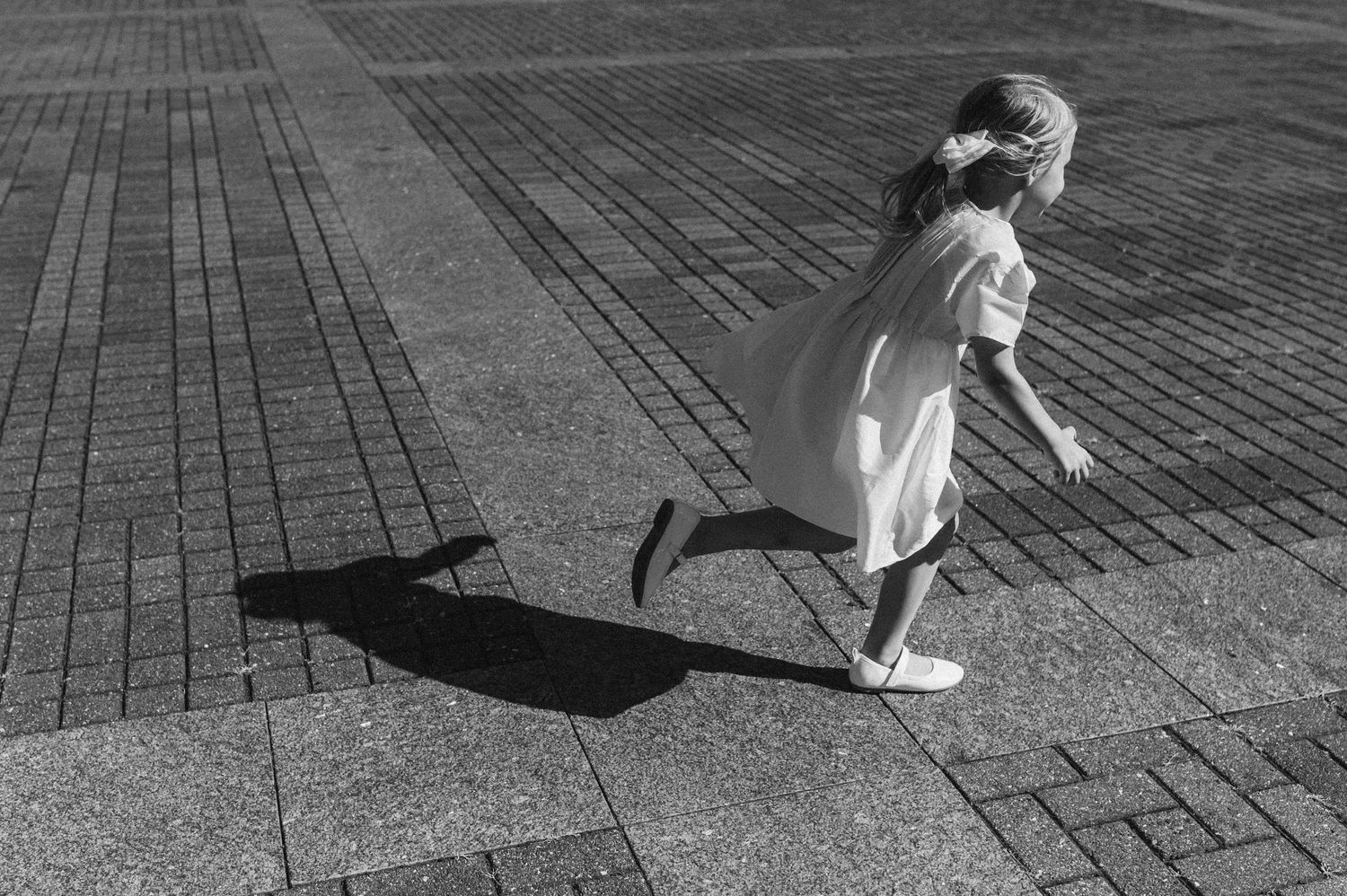 Black and white photo of small figure casting dramatic shadow on brick pavement.