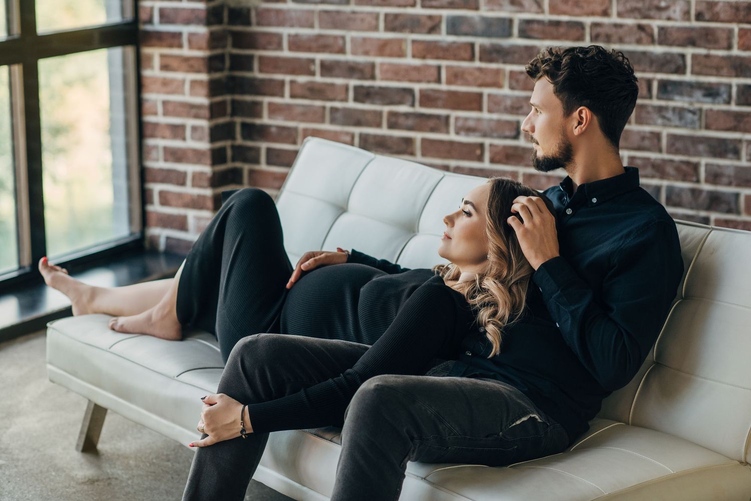 Couple relaxing on white sofa in casual black attire during intimate photoshoot.