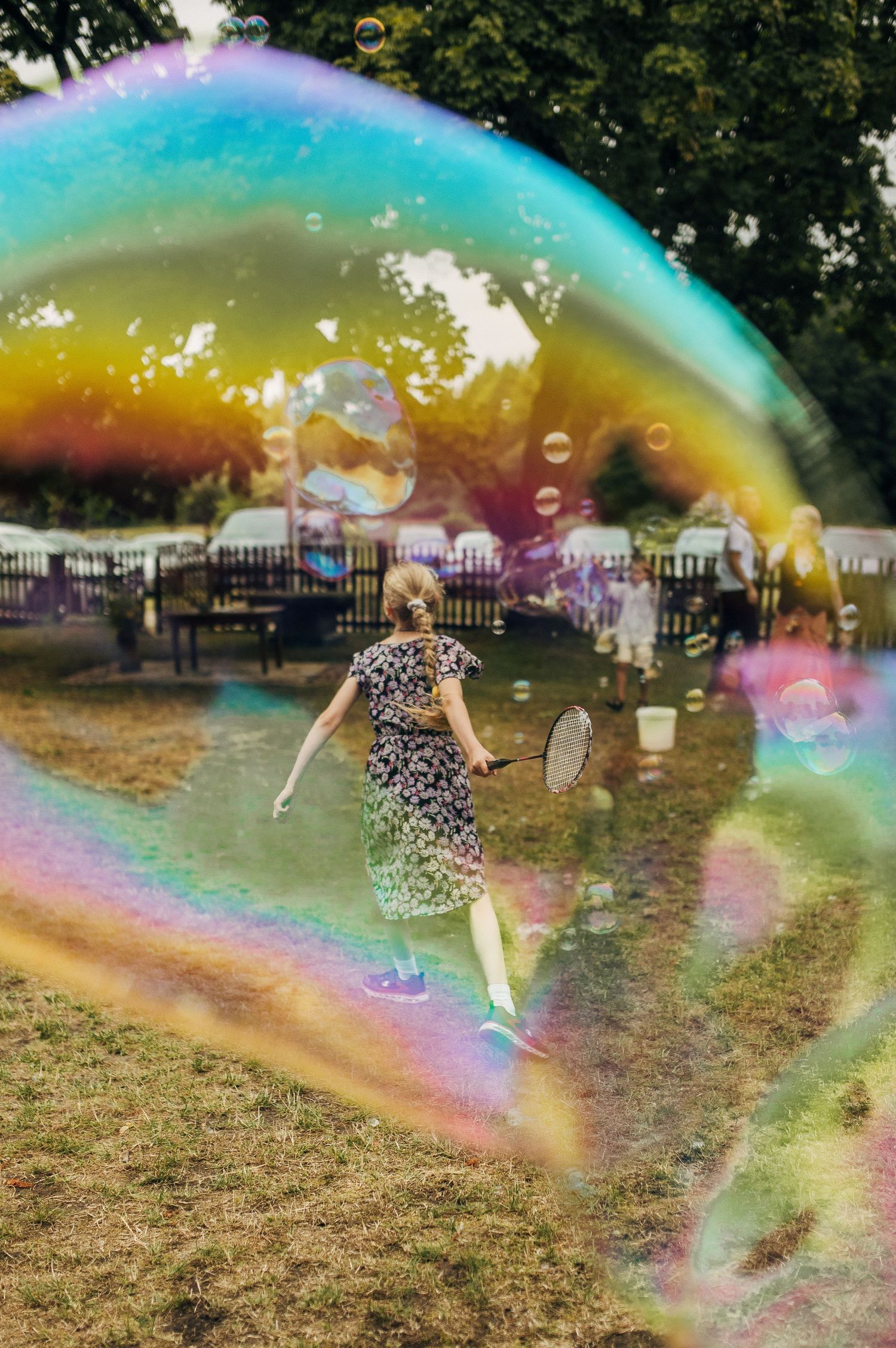 Girl playing badminton seen through a large colorful soap bubble outdoors.