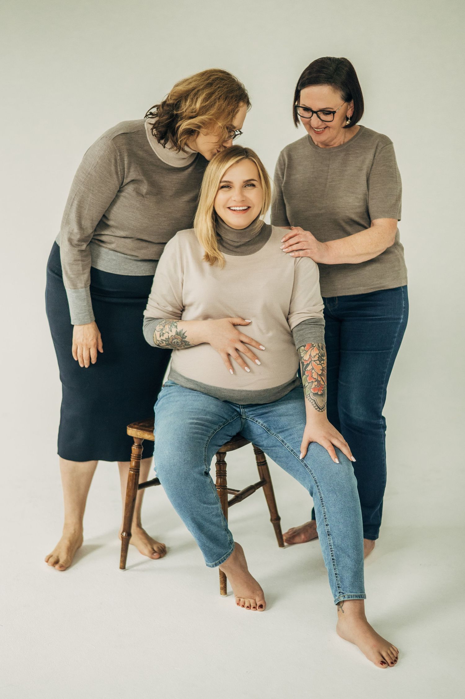 Three women share tender moment during casual maternity portrait session.