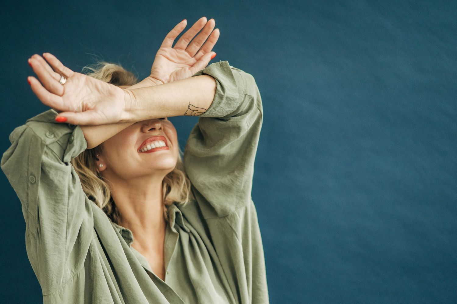 Woman in green shirt laughing with hands covering face against dark background.